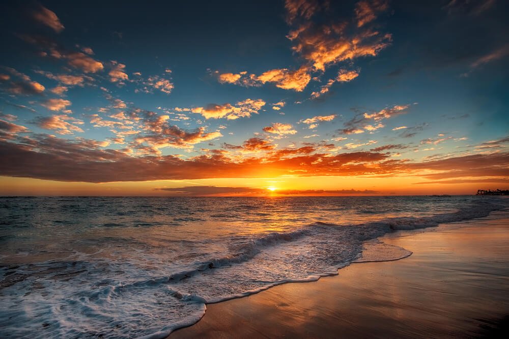 Sunset over the ocean with clouds in the sky, gentle waves on the sandy beach.