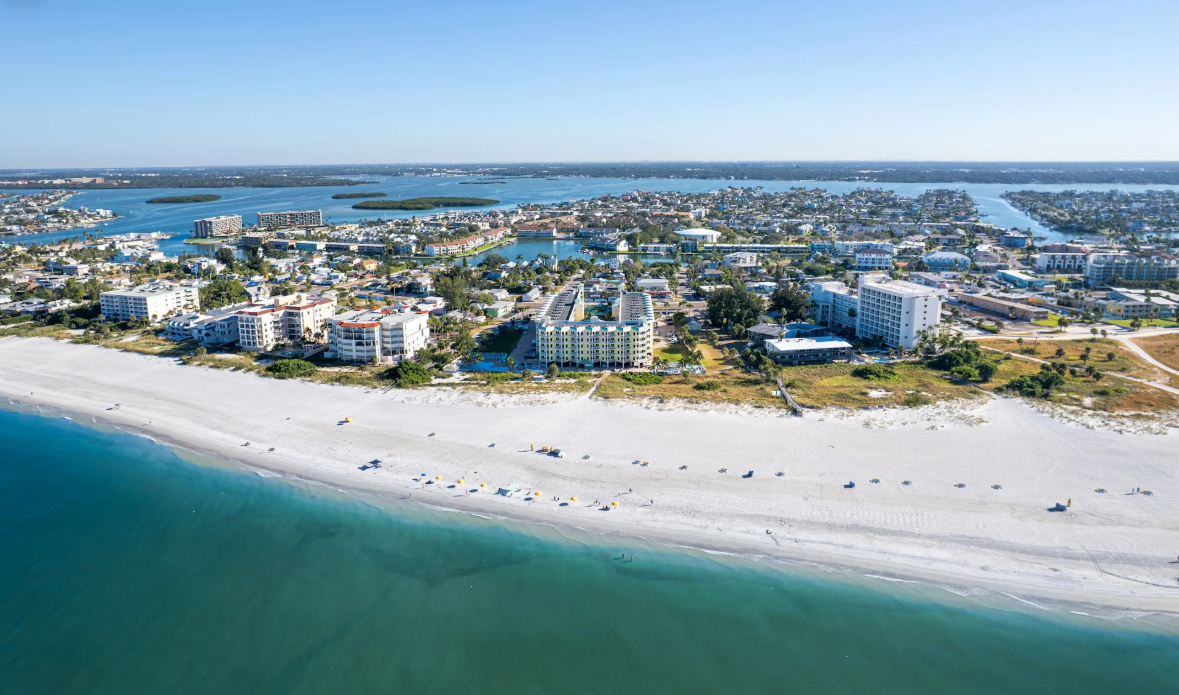 Aerial view of a coastal city with white sandy beach, beachfront buildings, and numerous lakes or rivers in the background.