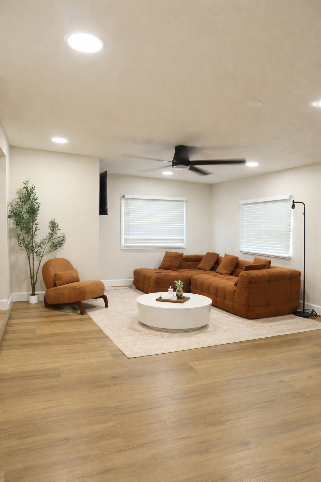 Living room with brown sectional sofa, matching armchair, white oval coffee table, indoor plant, and ceiling fan.