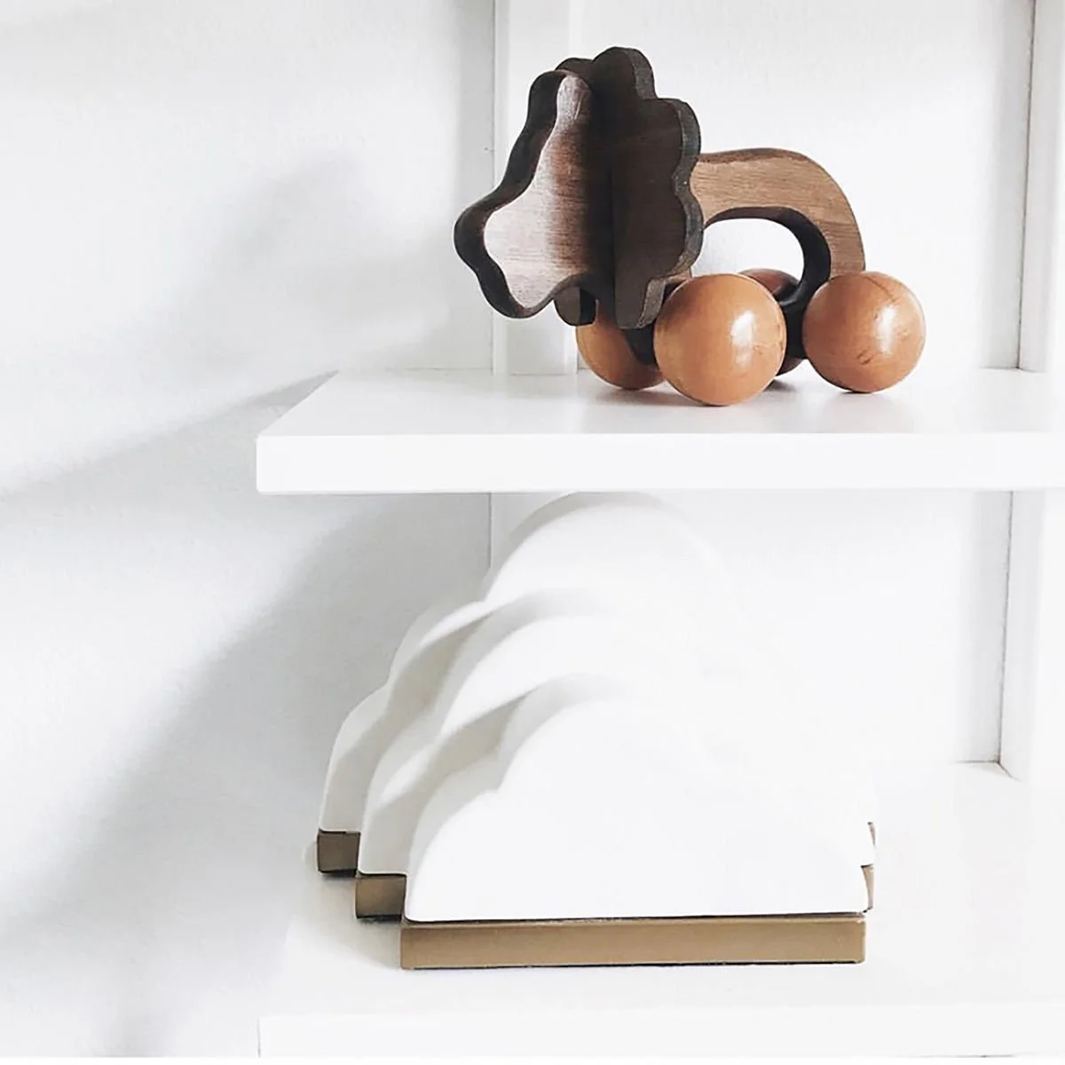 Decorative wooden toy car on a white shelf with white and beige bookend in front.