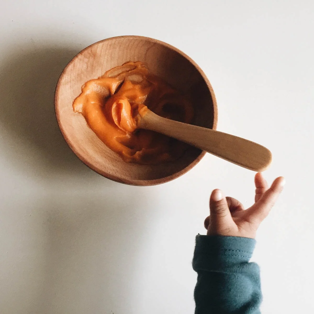 Child's hand reaching into a wooden bowl with caramel popcorn, holding a wooden spoon.