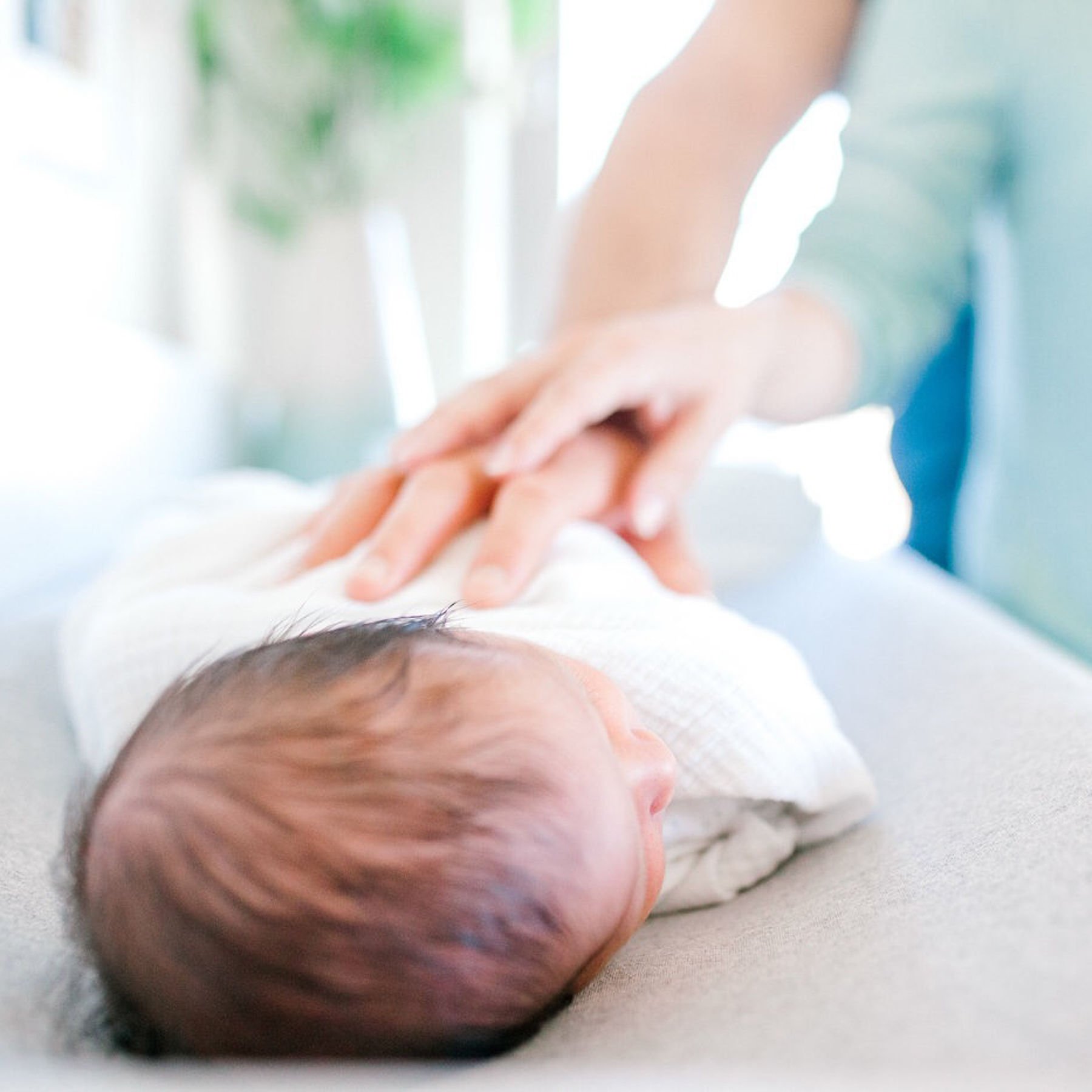 A newborn baby lying on a soft surface with a white blanket, getting a gentle massage from an adult's hands.
