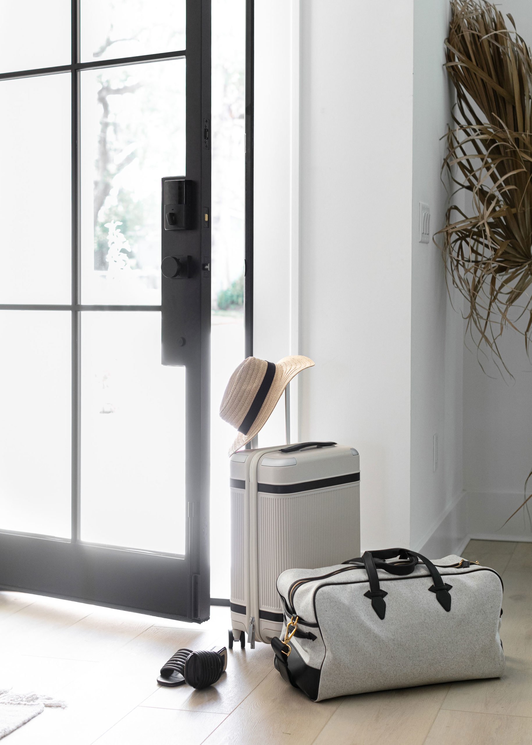 Indoor scene with a front door, luggage, a straw hat, and a pair of headphones on the light-colored floor near the door.