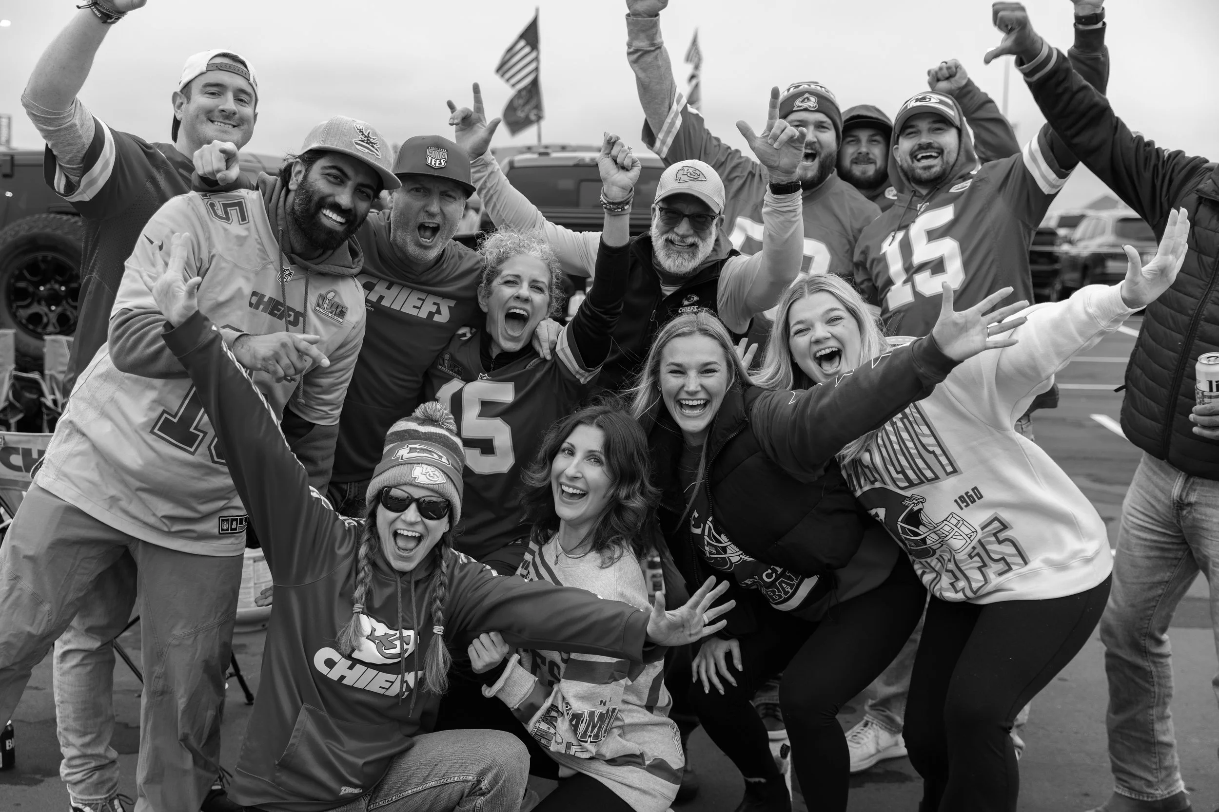 A group of excited sports fans wearing Kansas City Chiefs gear celebrating together outdoors.