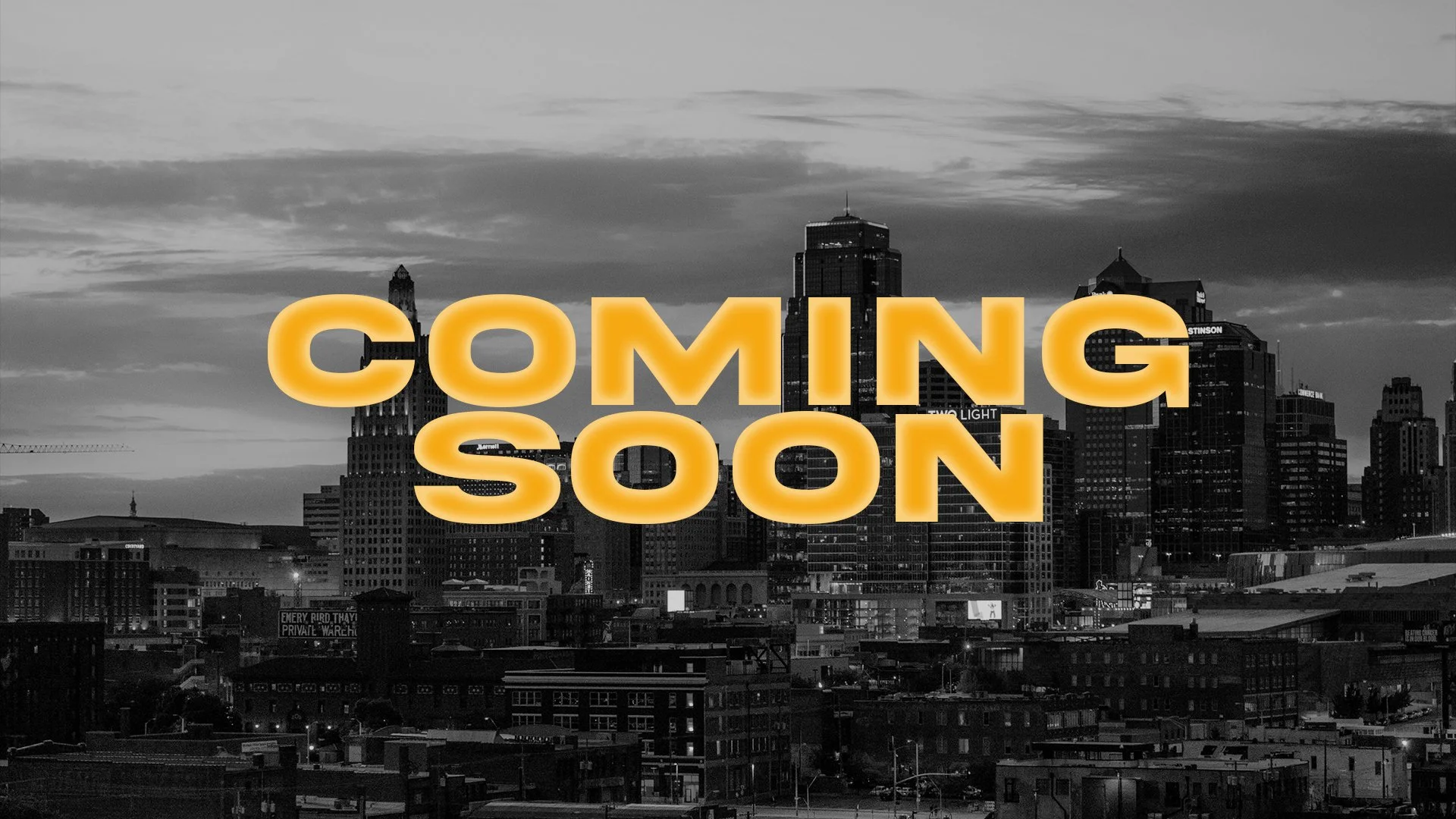 Black and white cityscape of downtown with tall buildings, overlaid with large orange text saying "Coming Soon".