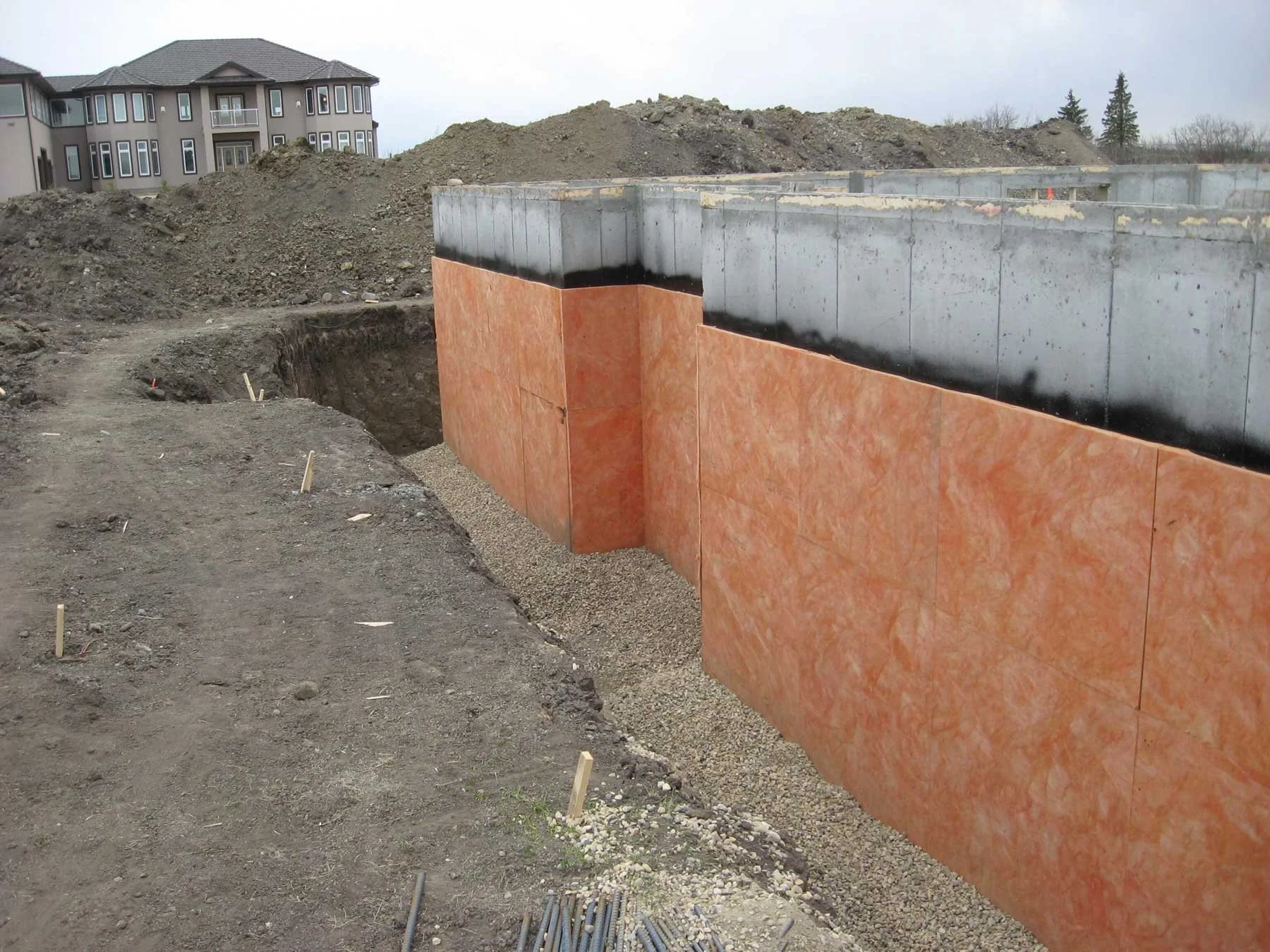 Foundation walls with waterproofing membrane and foam insulation boards installed prior to backfill on Edmonton-area new home construction.
