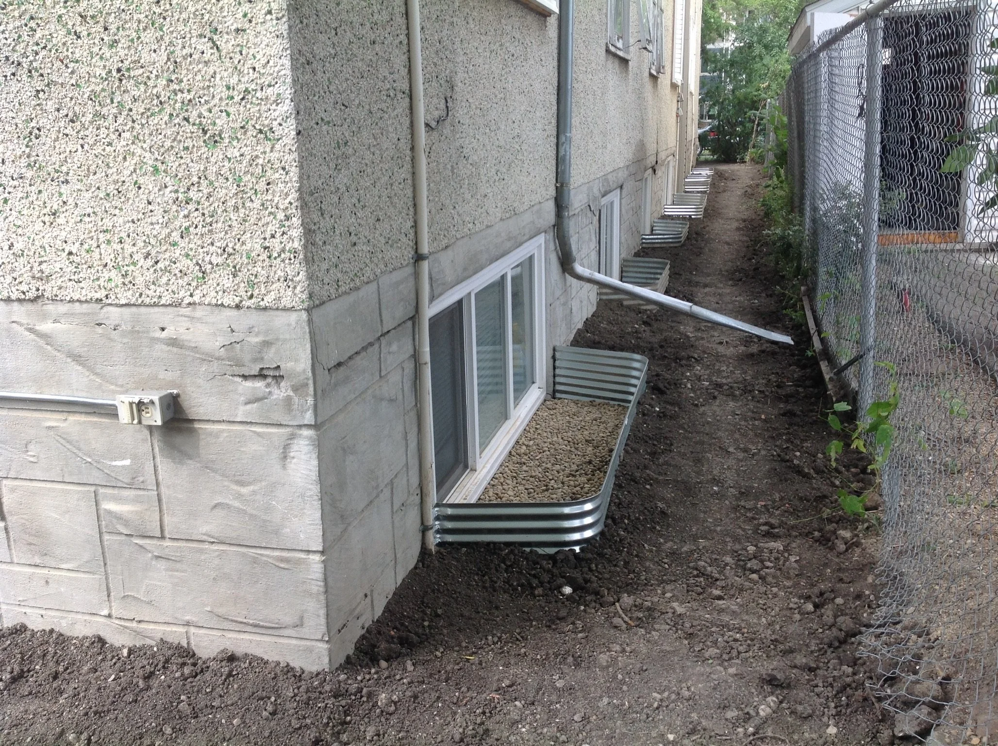 Double window well installation with galvanized metal surrounds and gravel drainage on a block foundation.