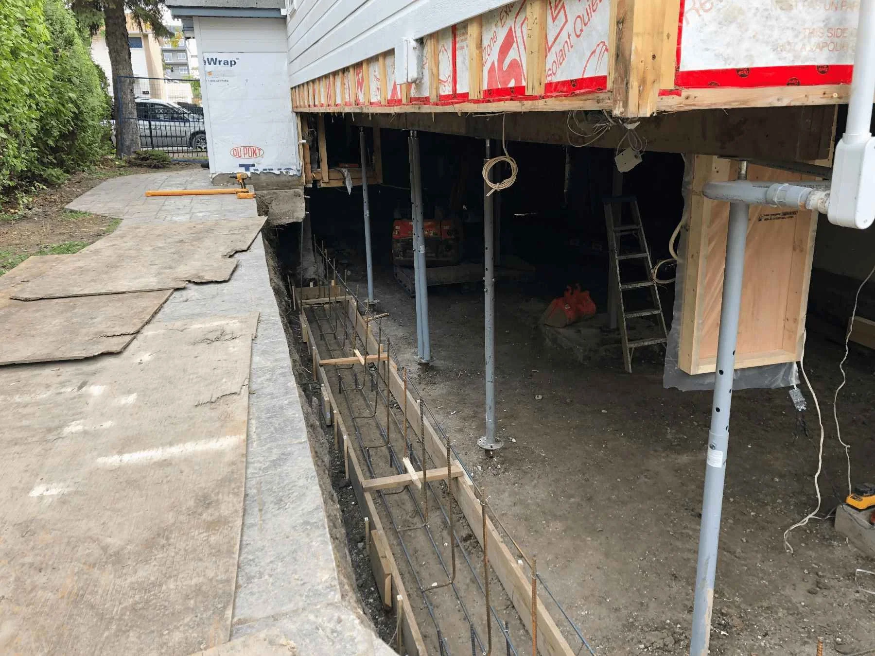 Home elevated on temporary supports with rebar placed in the excavated trench for new foundation walls.