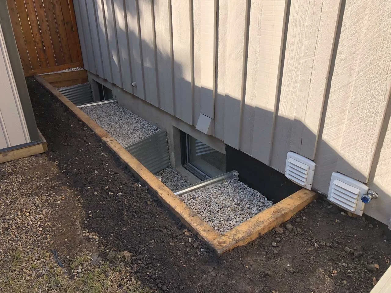 Window well installation with galvanized metal surround and gravel drainage base connected to weeping tile system.