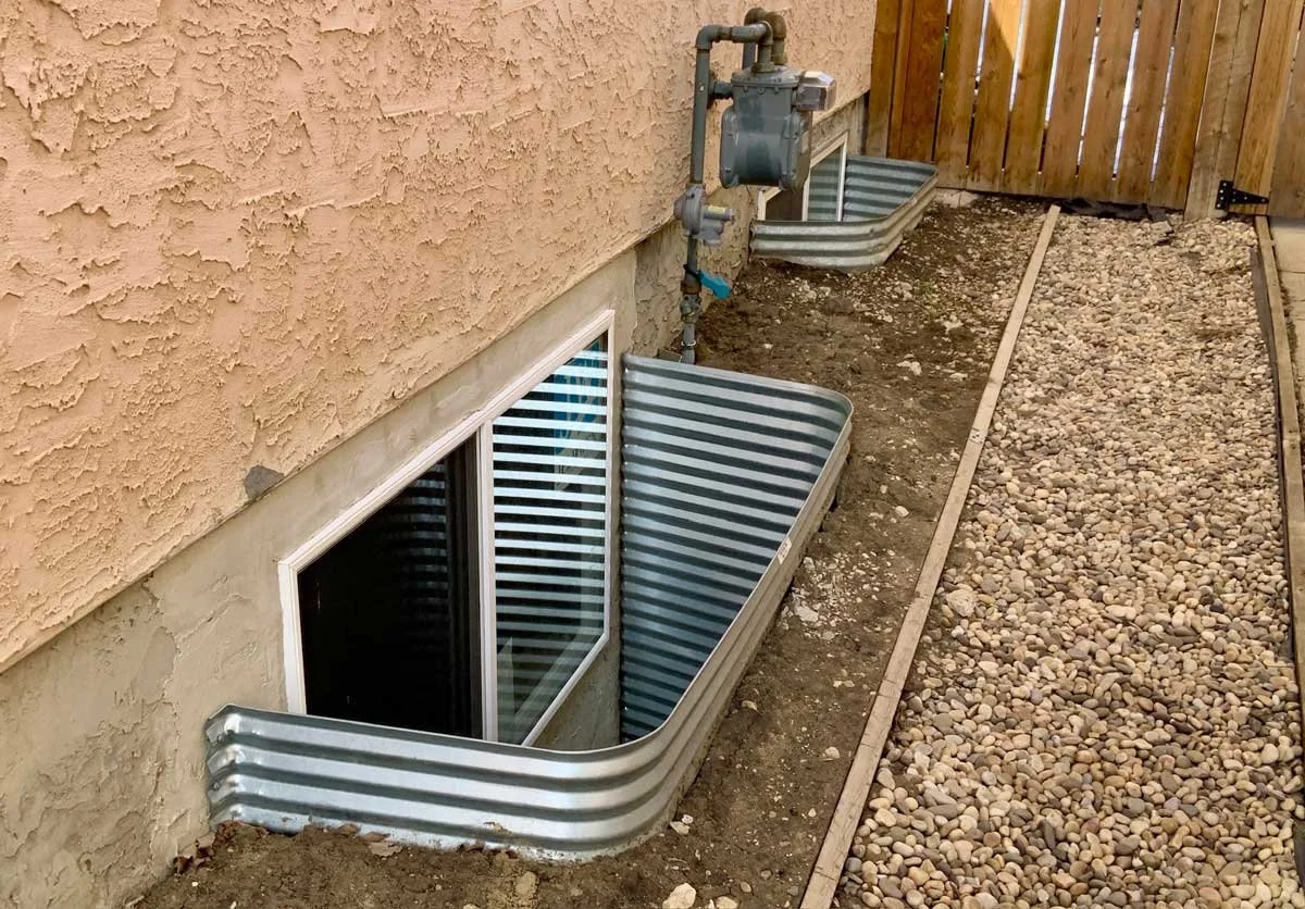 Large circular egress window well with galvanized surround installed beside the home.