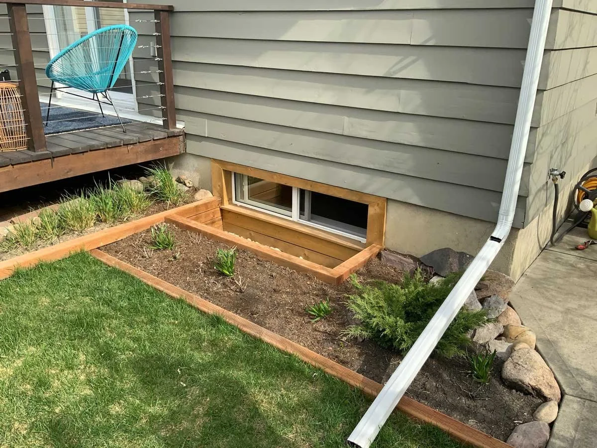 Custom window well with cedar wood frame and gravel base for drainage.