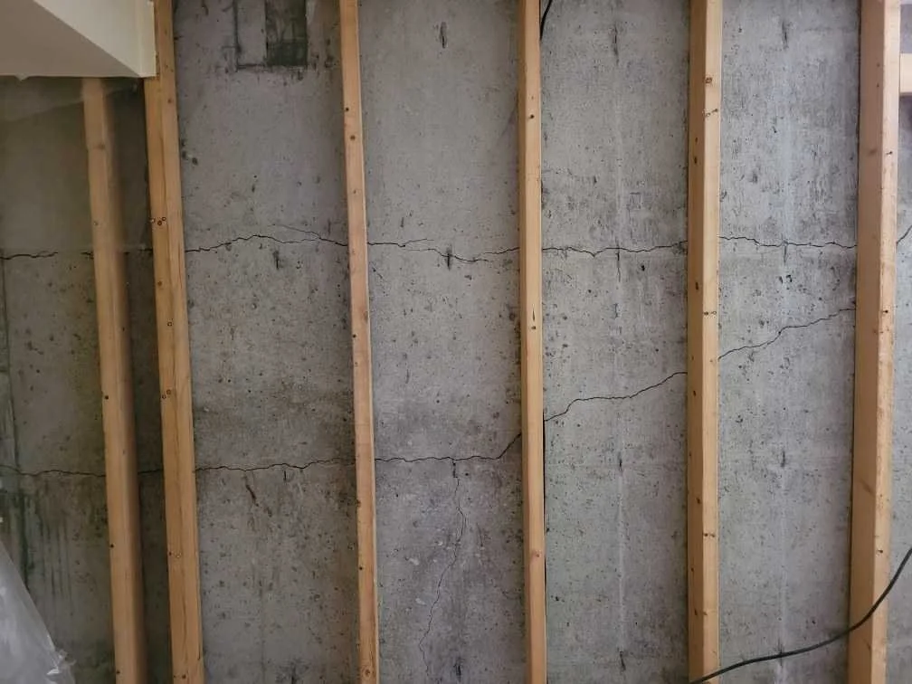 Interior wall with exposed wooden studs and cracked concrete wall.