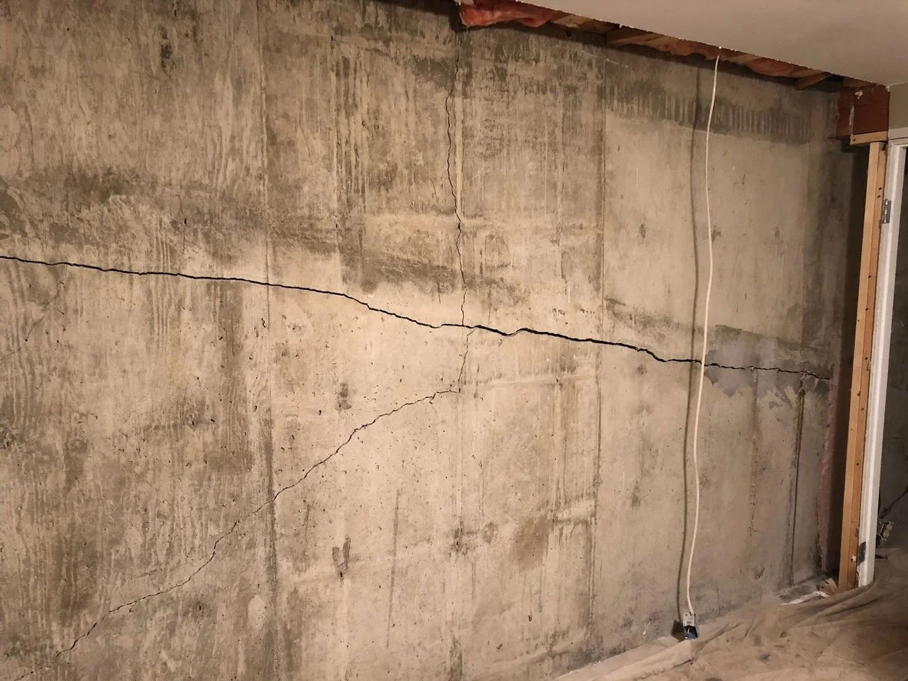 Cracked concrete wall under renovation with exposed framing and a white electrical cord hanging.