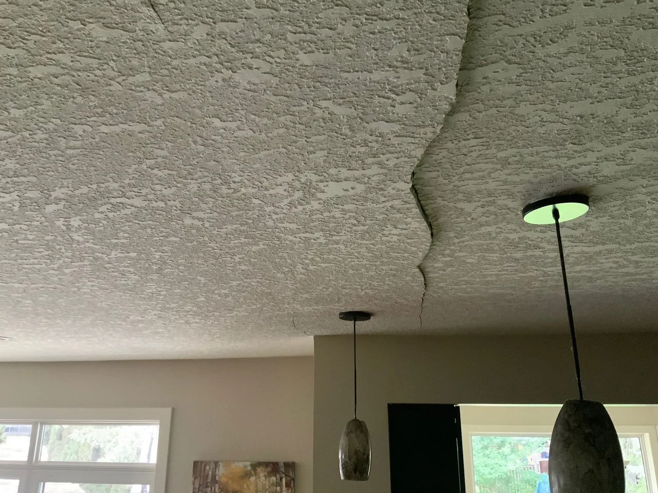 Ceiling with a severe crack running across it, two pendant lights hanging down, and a window letting in natural light in a room.