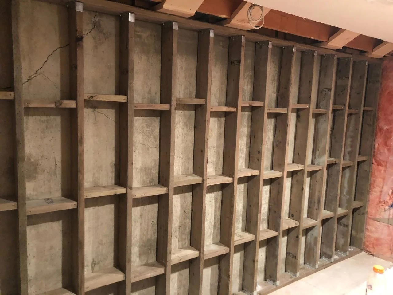 Pressure-treated wood stud wall bracing an existing foundation from the interior.