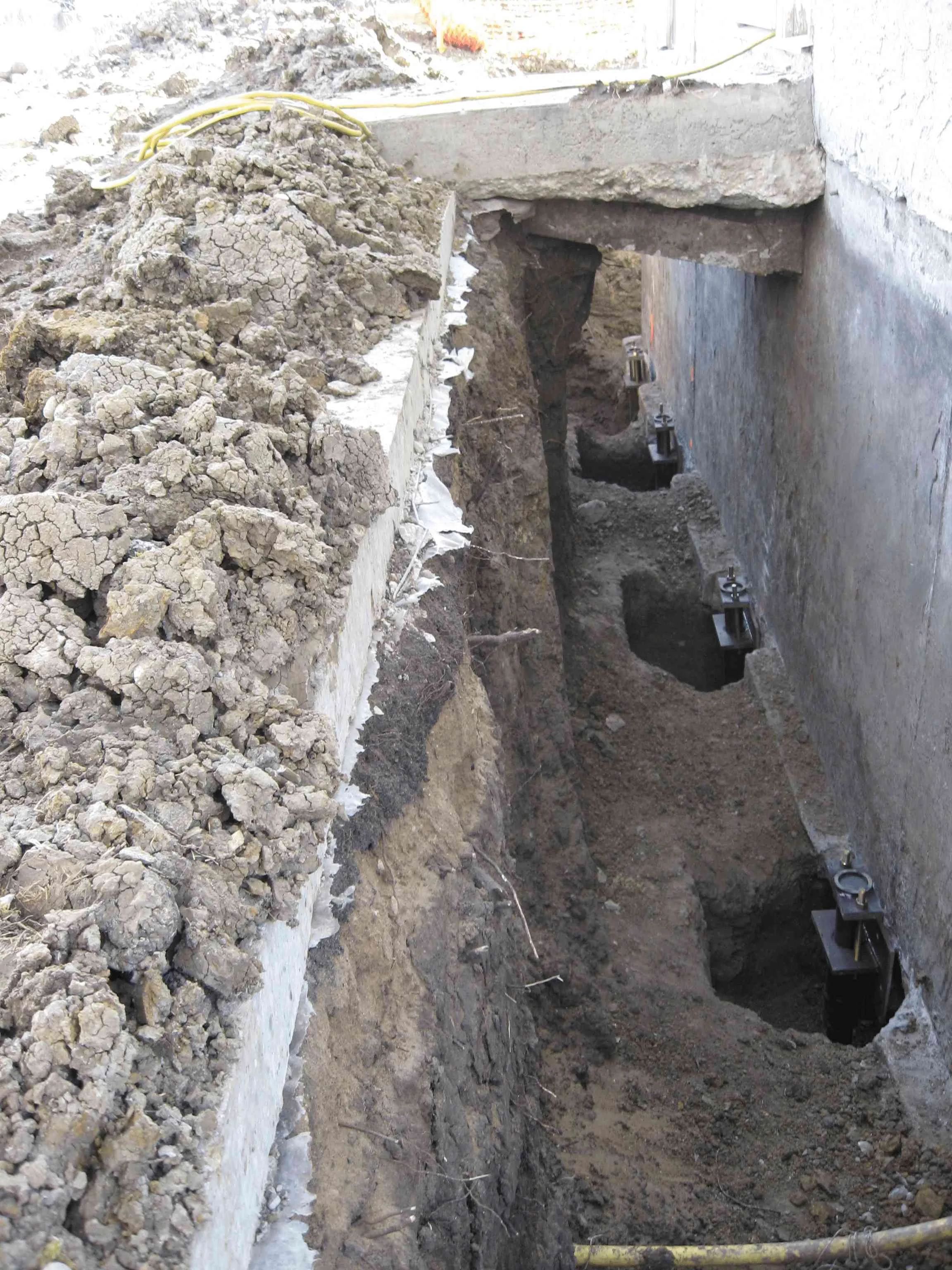 Multiple pier brackets installed in an excavated trench to support a settling foundation.