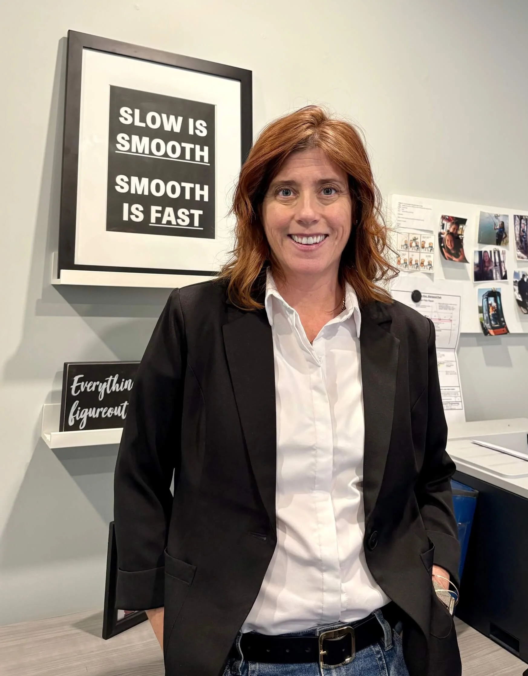 Rachelle Sutherland in a black blazer and white shirt standing in front of a wall with motivational quotes and photos.