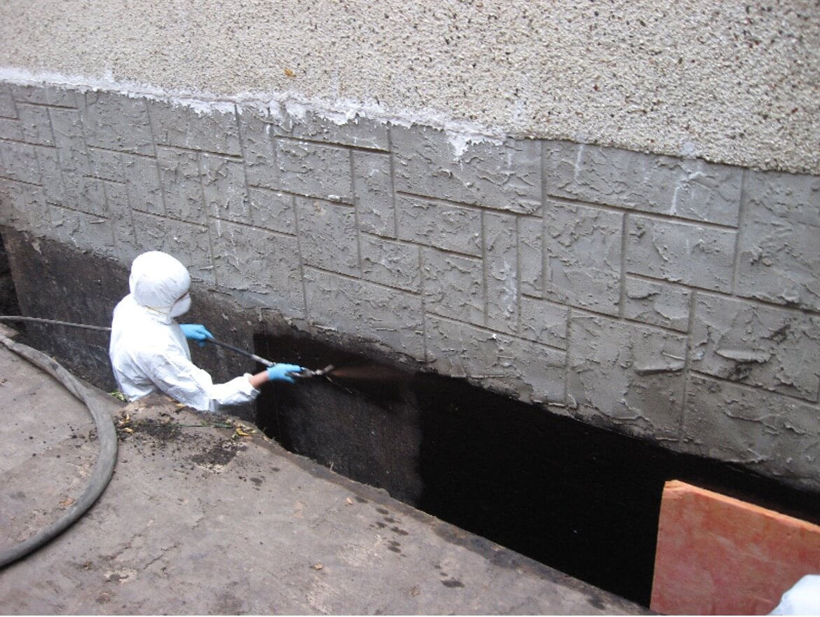 Technician applying TUFF-N-DRI elastomeric waterproofing membrane to an excavated foundation wall.