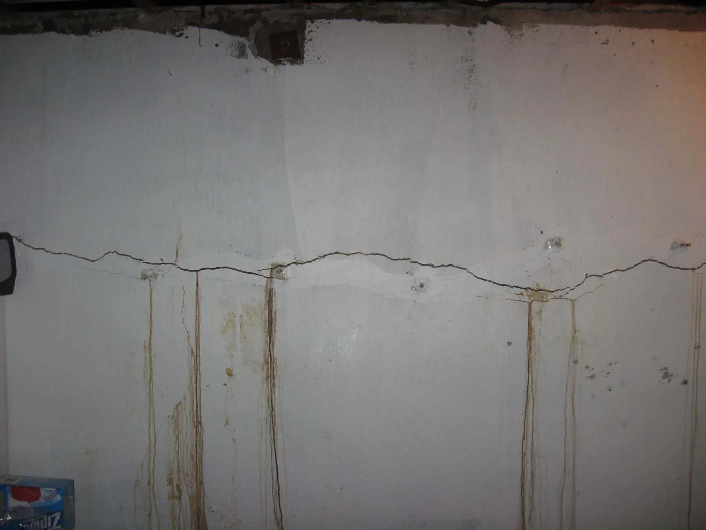 A wall with a large crack running horizontally and several vertical stains below the crack.