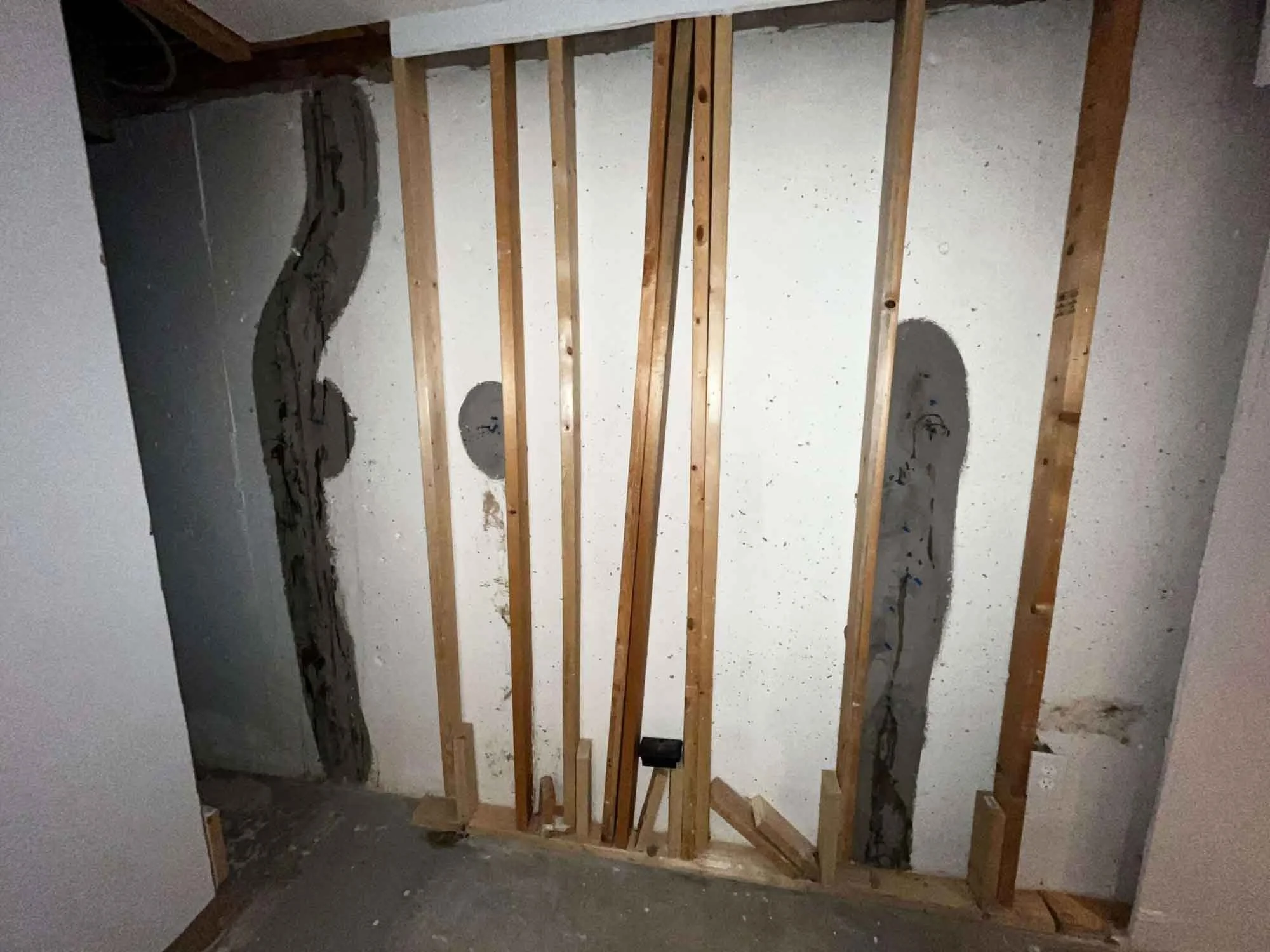 Basement wall with exposed wood framing showing multiple foundation crack repairs sealed with resin injection from the interior.