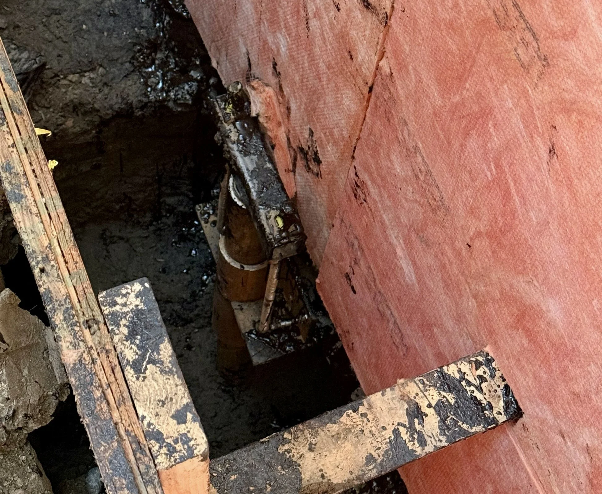 Pier bracket installation beside rigid foam insulation on an excavated foundation wall.
