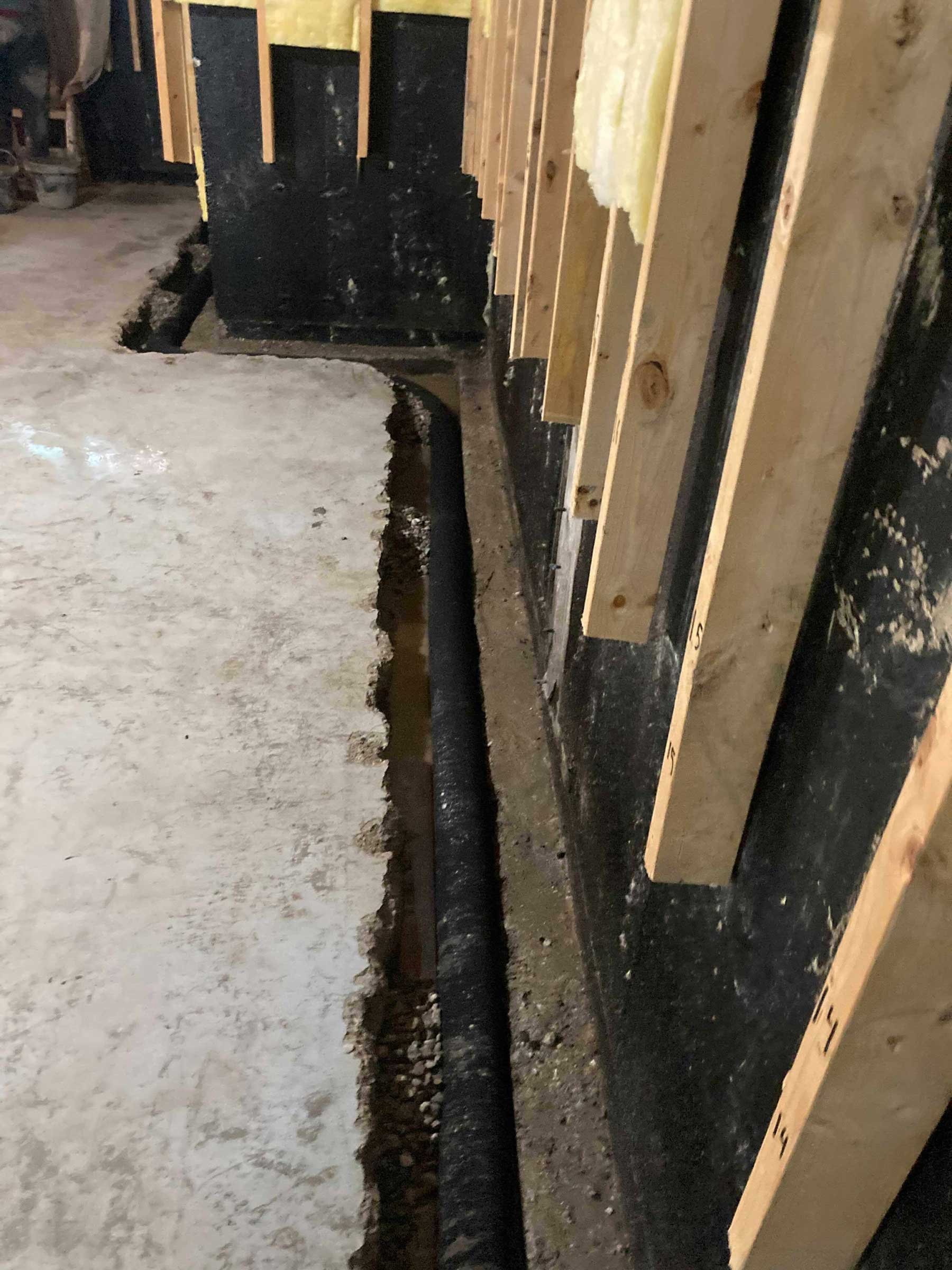 Interior weeping tile installation in a basement, with perimeter trench cut along the foundation wall and drainage pipe placed alongside the footing.