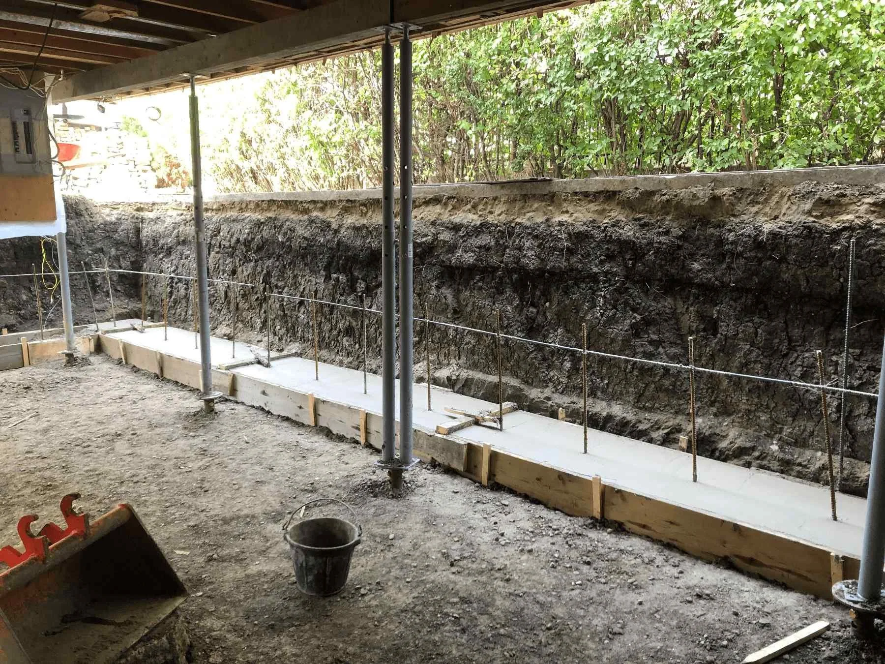Excavation beneath a home with floor joists exposed during foundation replacement to increase basement height.