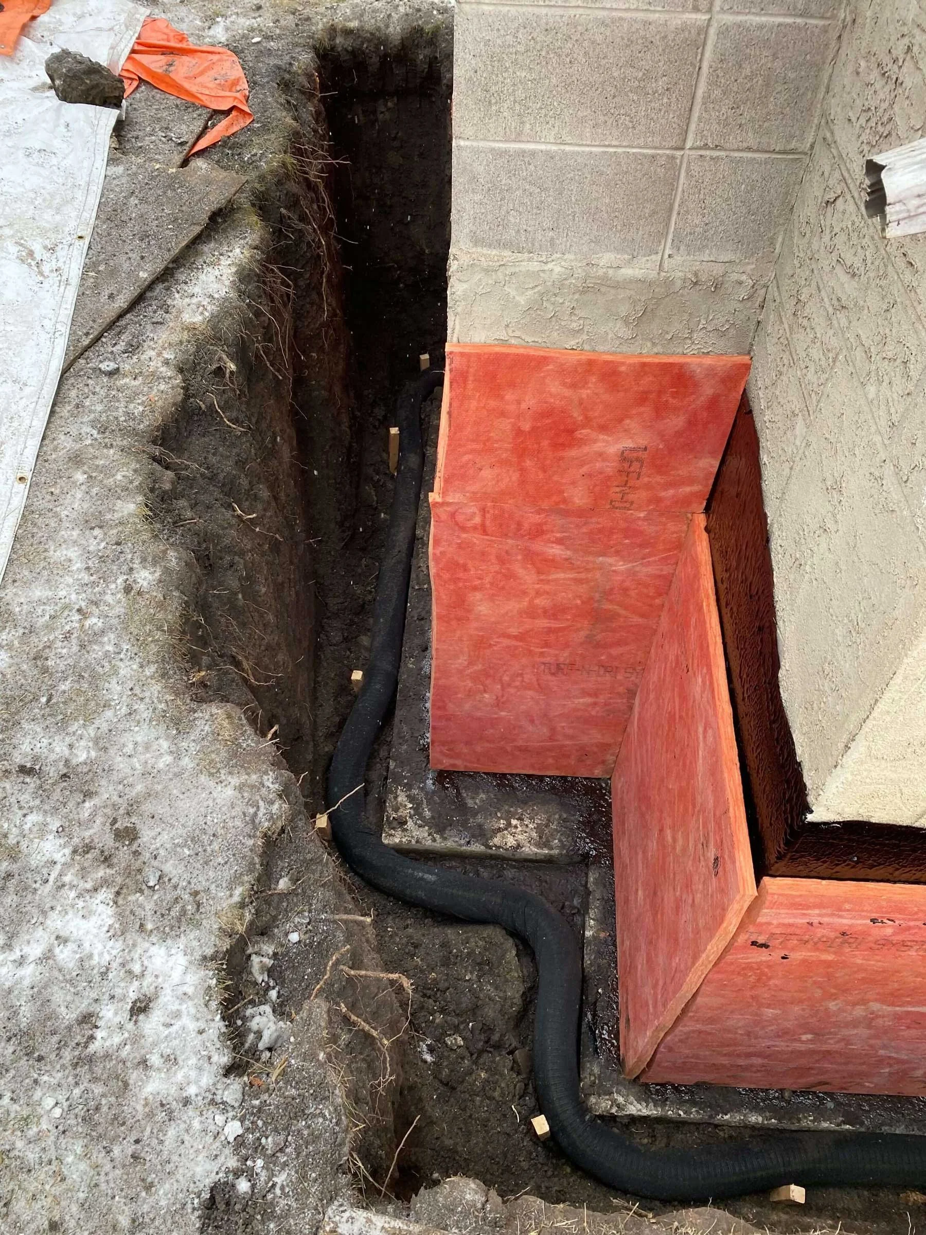 Modern perforated weeping tile installed along the foundation footing, with rigid foam insulation board protecting the exterior foundation wall.