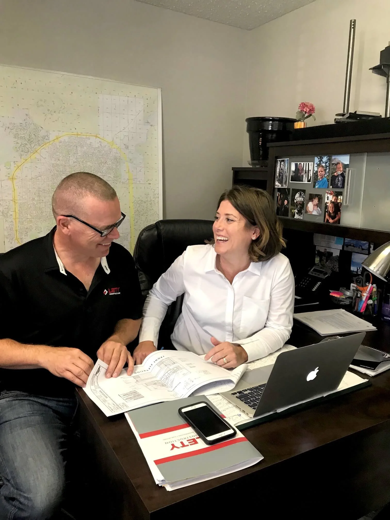 Rachelle and Wes Sutherland, owners of LETY Construction, smiling and reviewing a document together at their office desk.