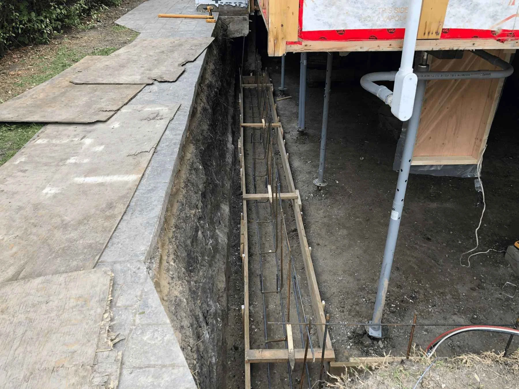 Rebar reinforcement grid in place at a foundation corner with waterproofing membrane applied before pouring new concrete.