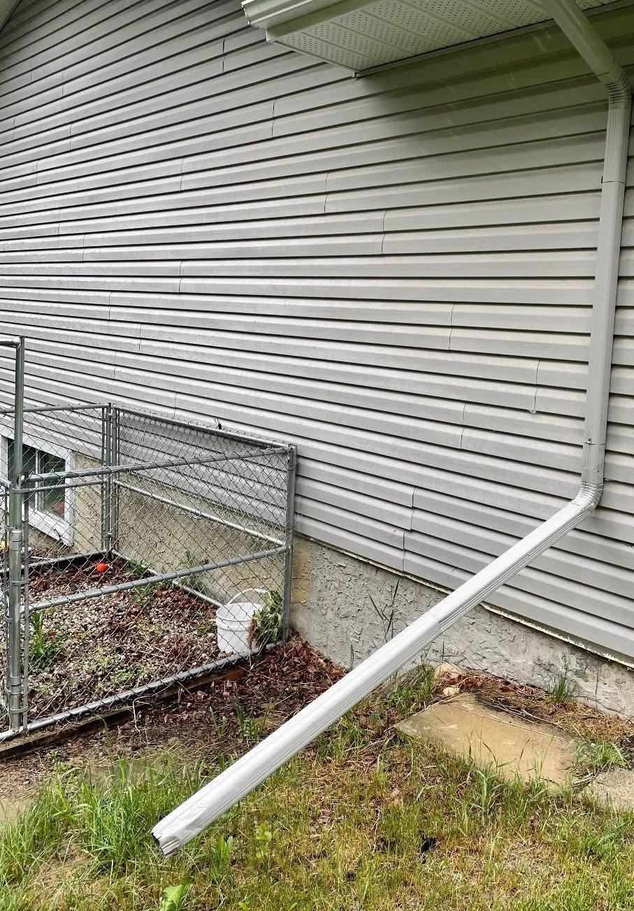 Downspout with extension directing water away from the foundation along the side of a home.