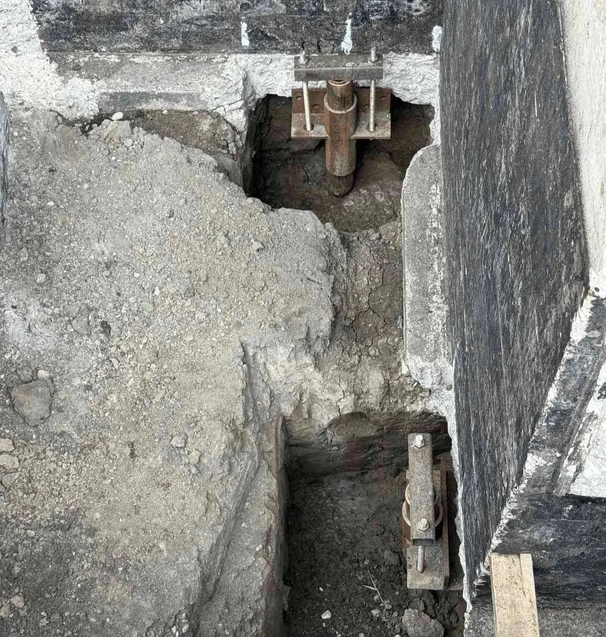 Helical pier bracket installed beneath a foundation footing during underpinning to stabilize and support a settling home.