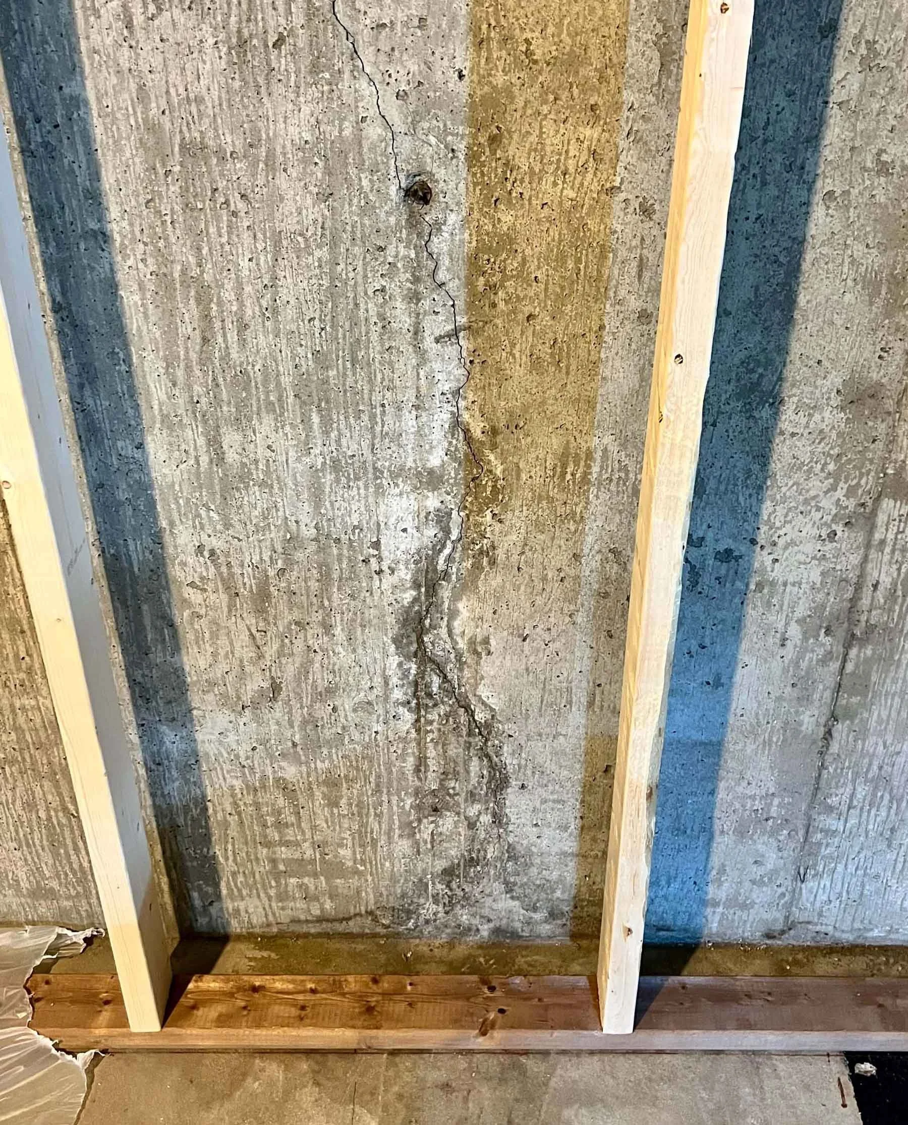 Concrete wall with visible cracks and uneven texture, framed by wooden studs, on a construction site.