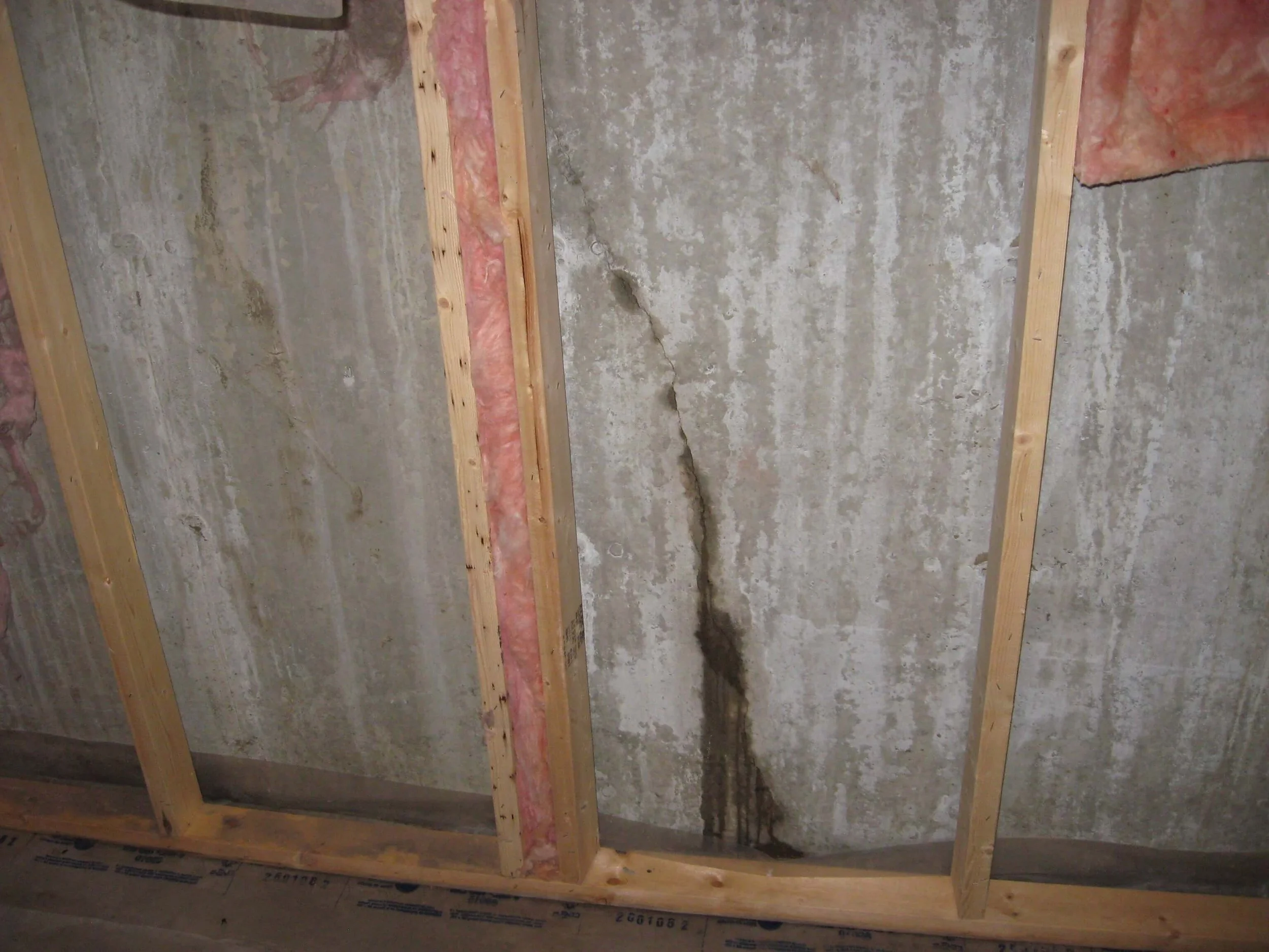 Crack in a concrete basement wall with water stain at the bottom.