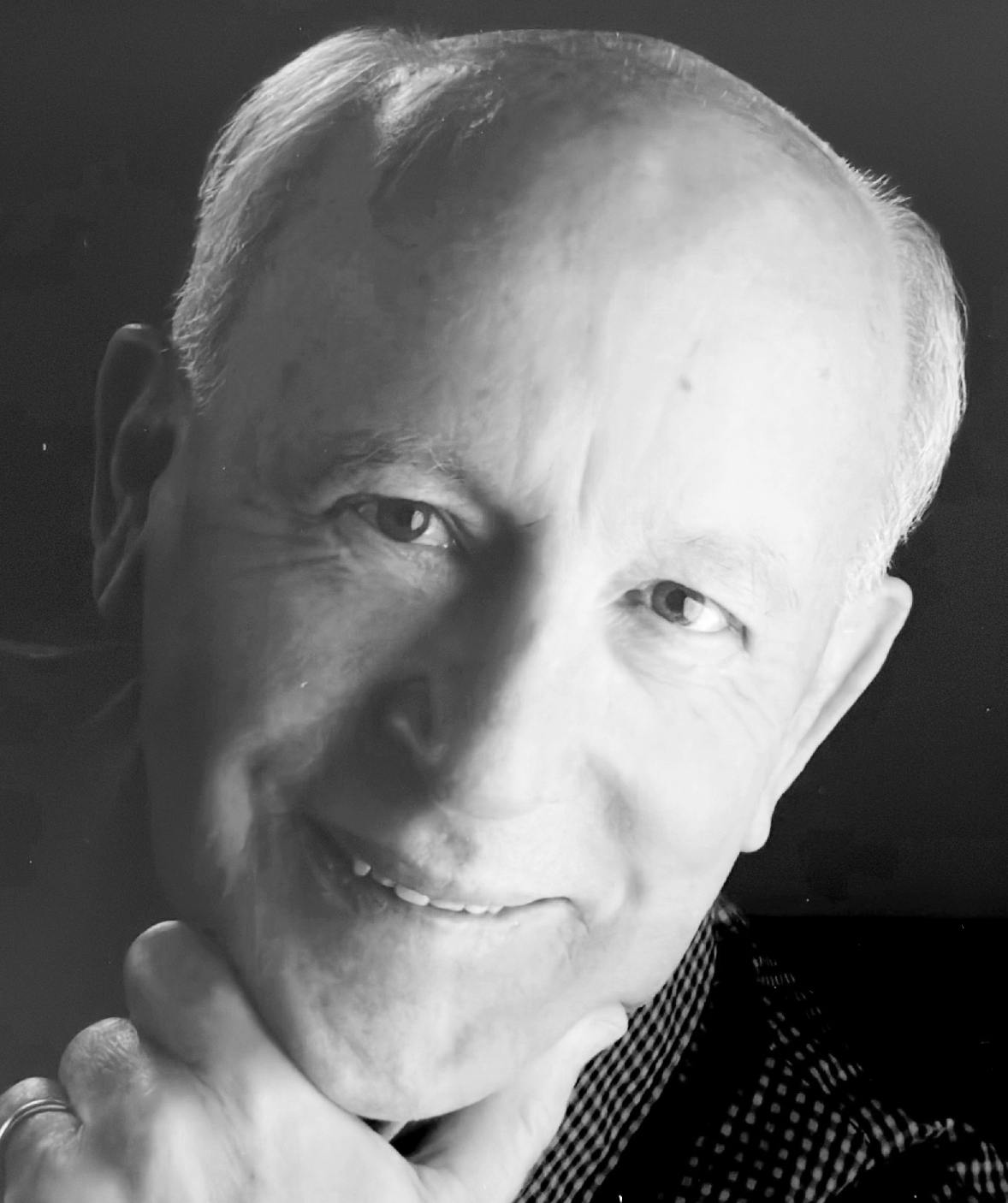 Black and white close-up portrait of an elderly man smiling, with his hand resting on his chin.