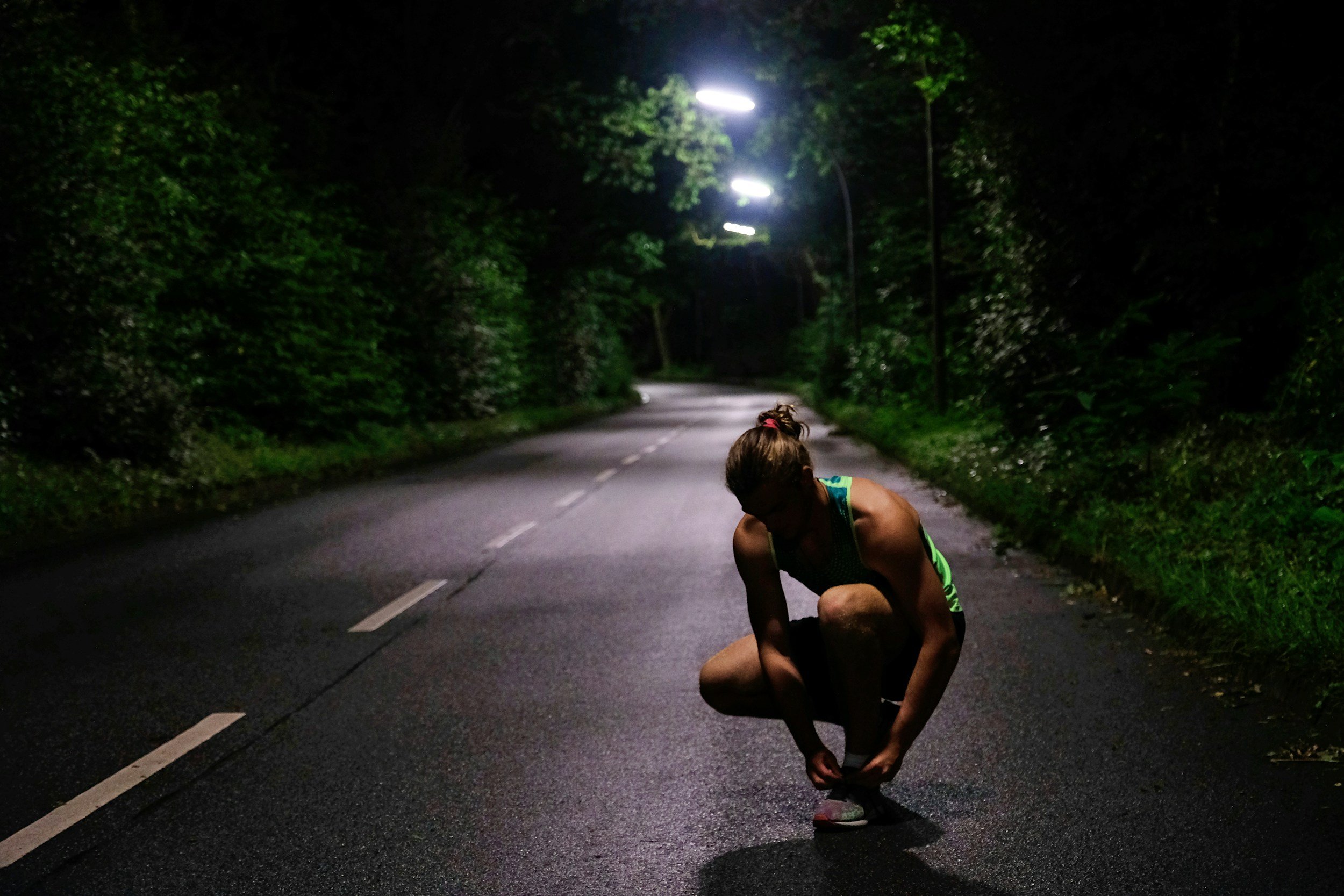 Woman tying shoe laces while running down a dark road