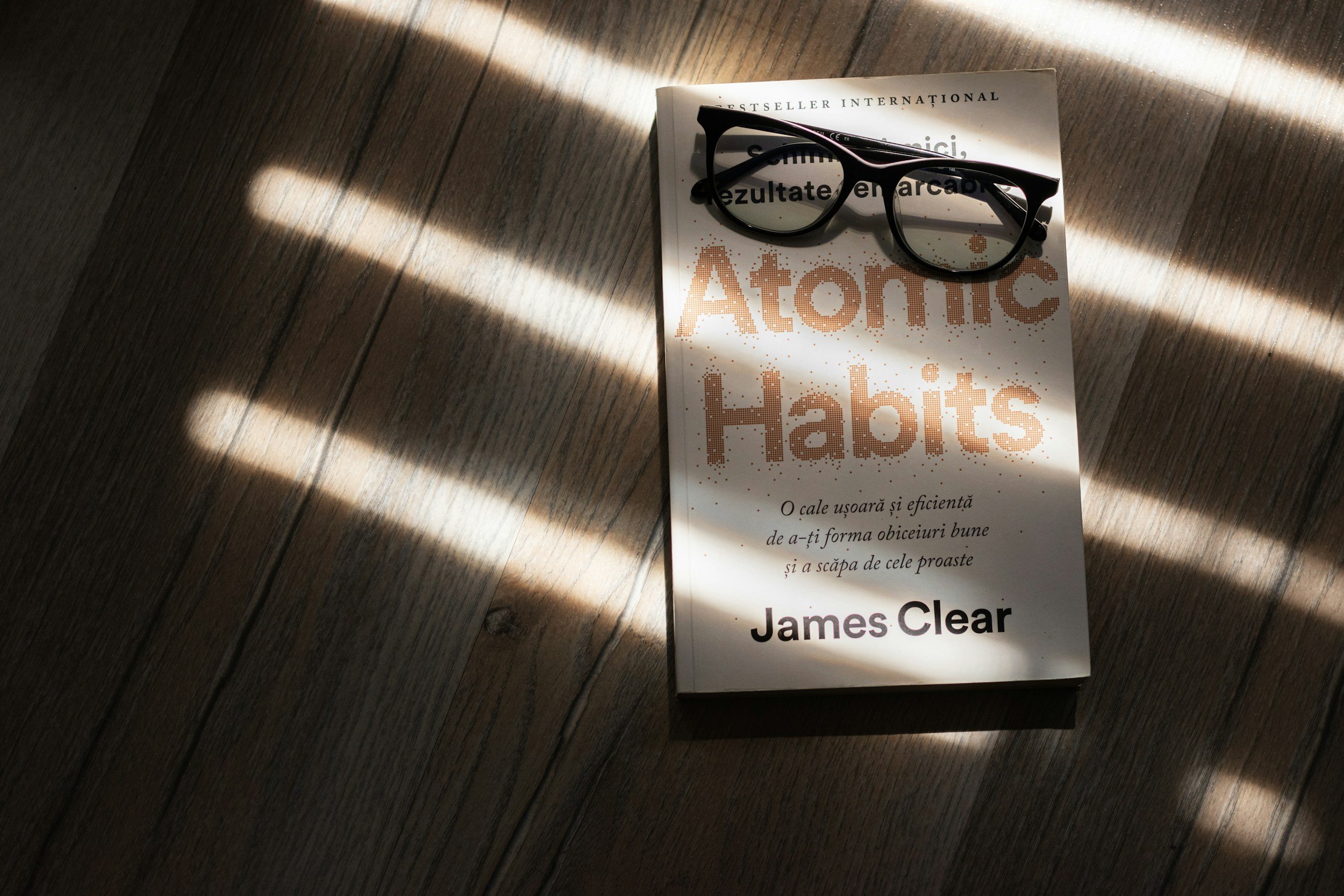 Atomic Habits by James Clear book with glasses on wood table