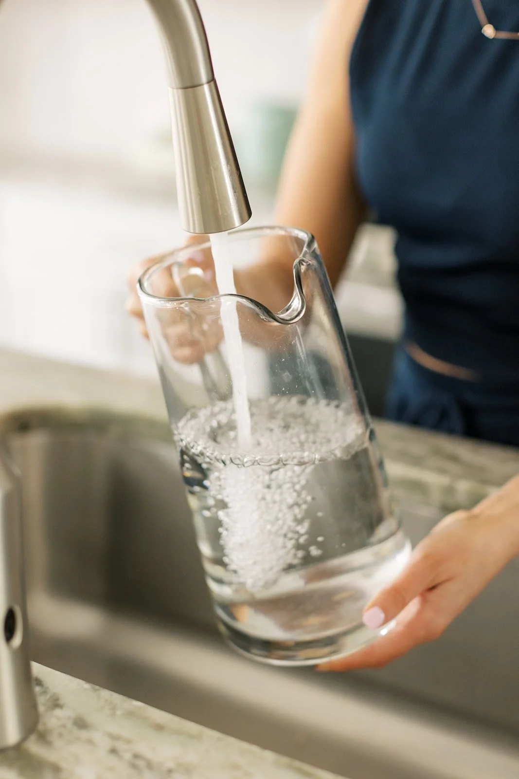 A person filling a glass with water from a modern kitchen faucet.
