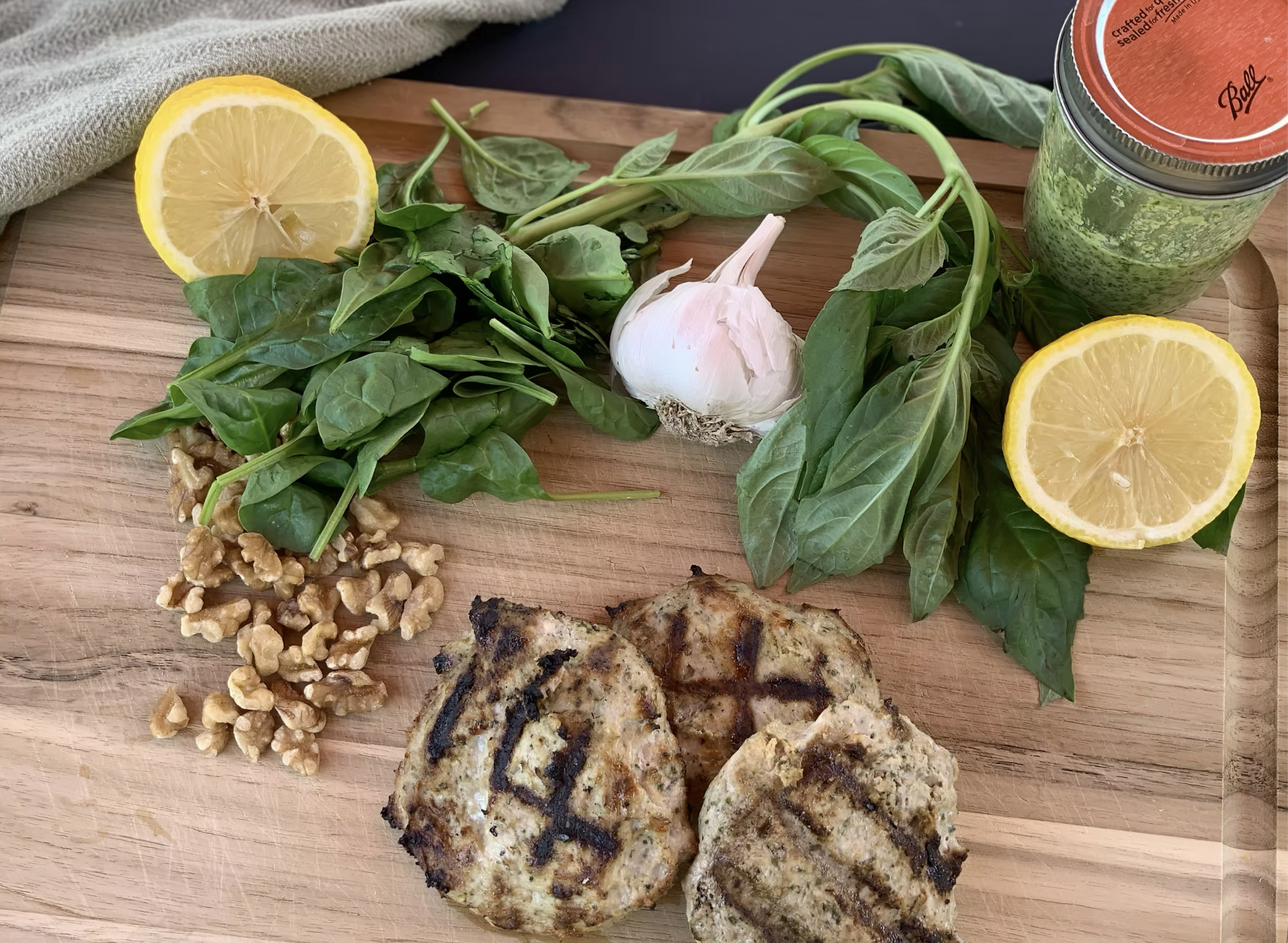 Grilled lemon pesto chicken burgers on cutting board with ingredients