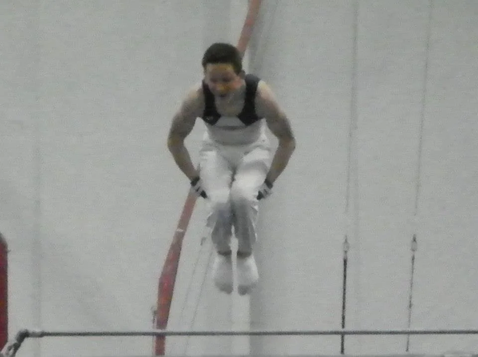 A person in athletic clothing performing a high jump over a bar in an indoor gymnasium.