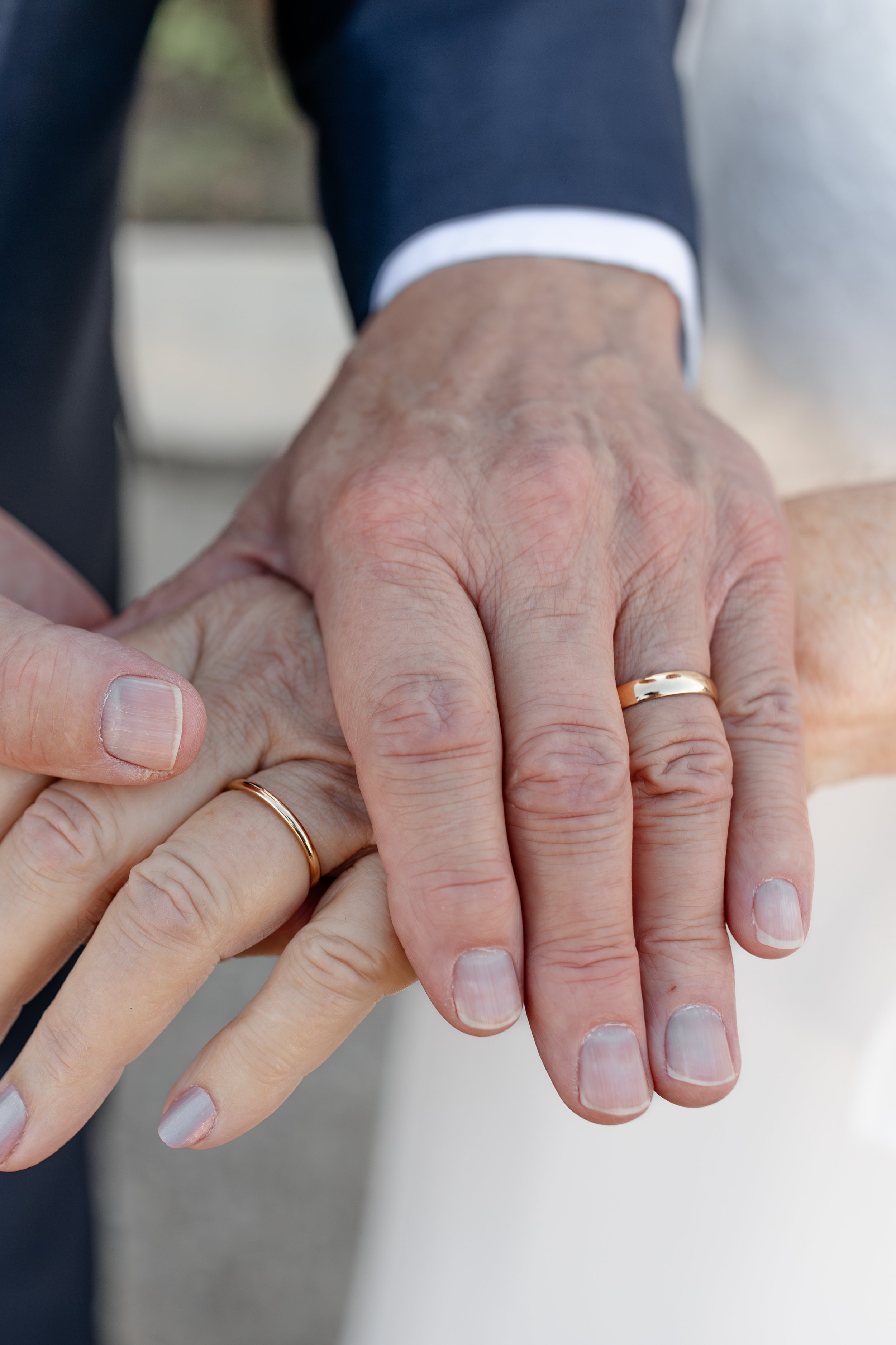 Close-up of two hands with wedding rings, one older and one younger, placed together in a gesture of unity.
