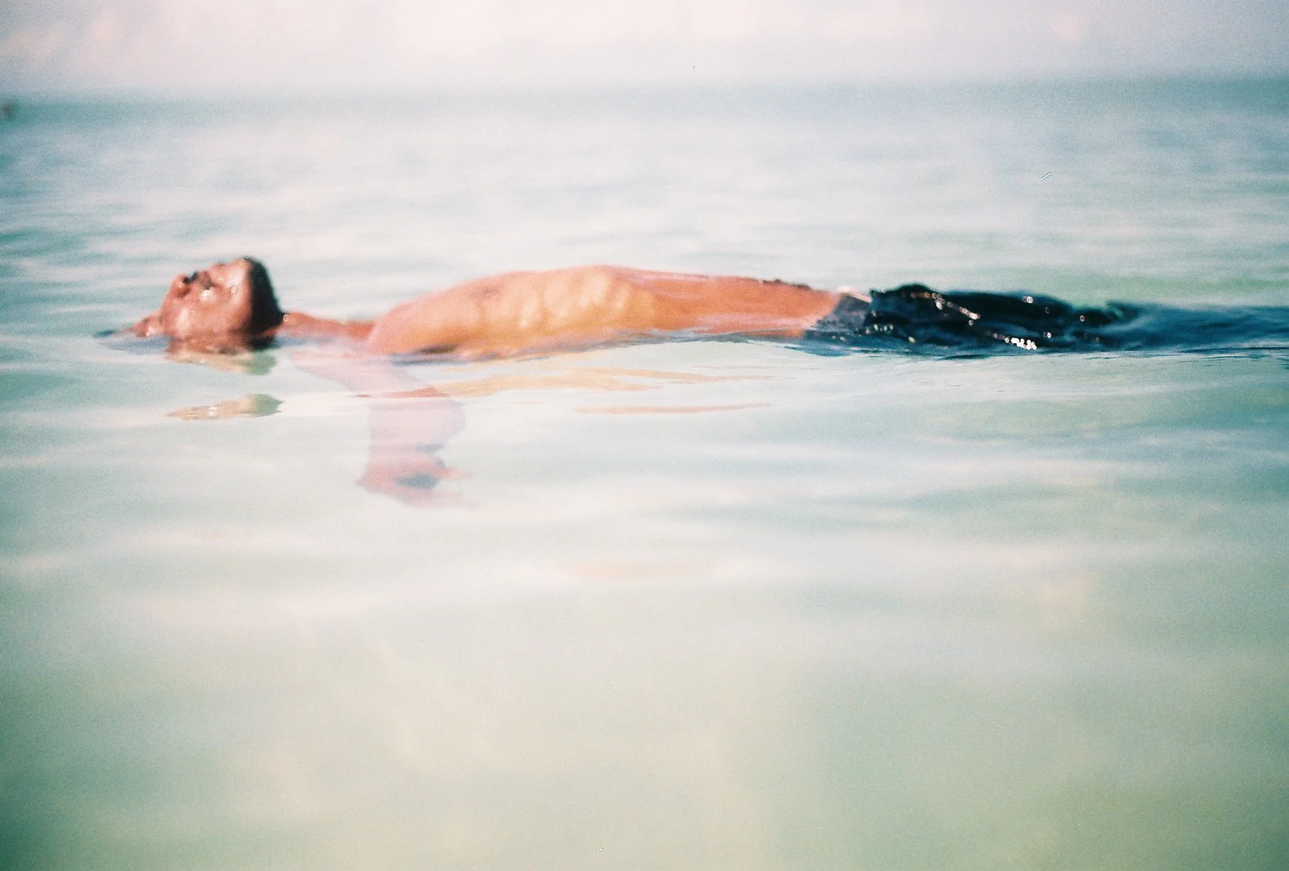 Person floating on their back in calm water with clear skies.