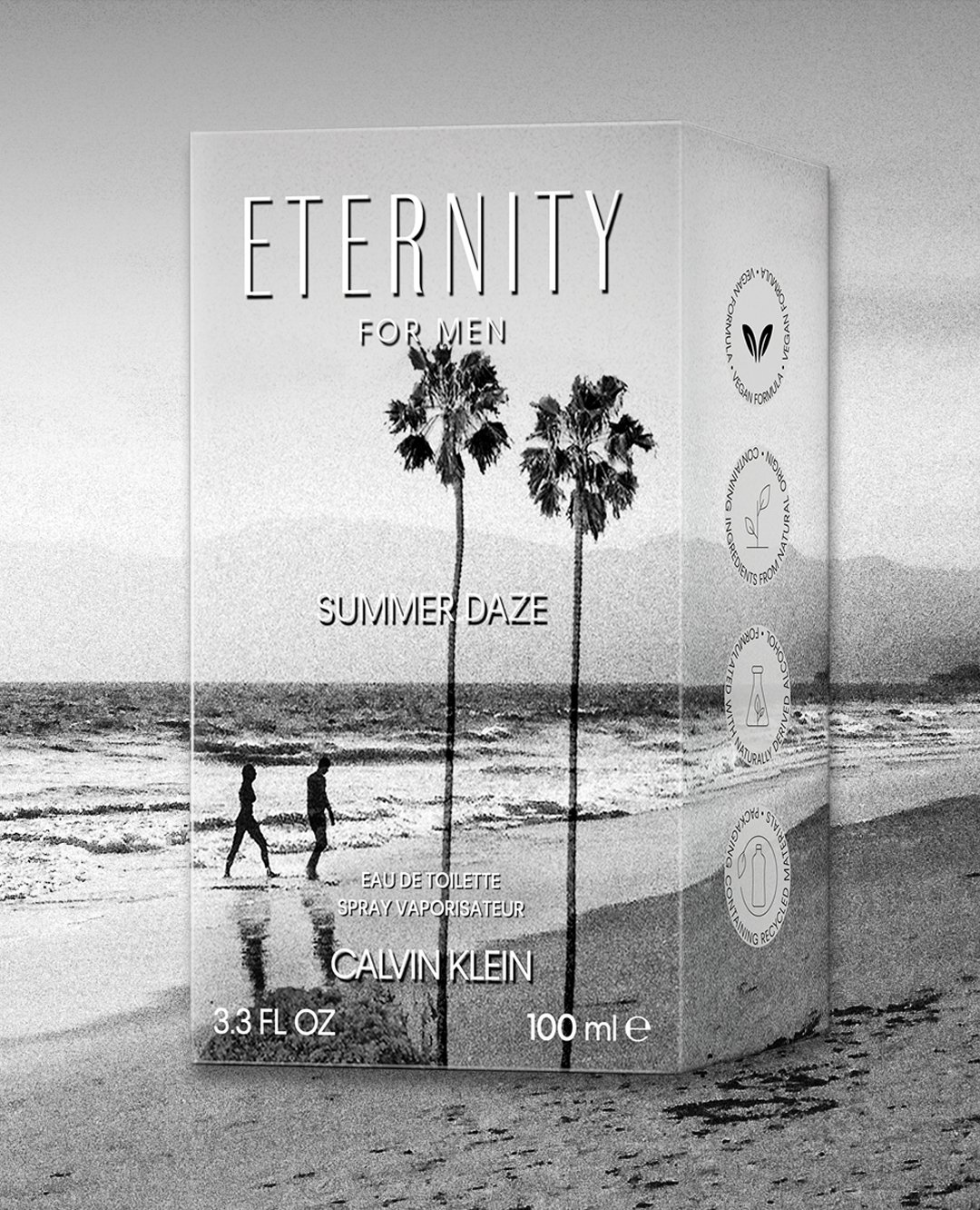 A black-and-white image of a perfume box labeled 'Eternity for Men Summer Daze' by Calvin Klein. The box shows two palm trees and a beach scene with two people walking along the shoreline.