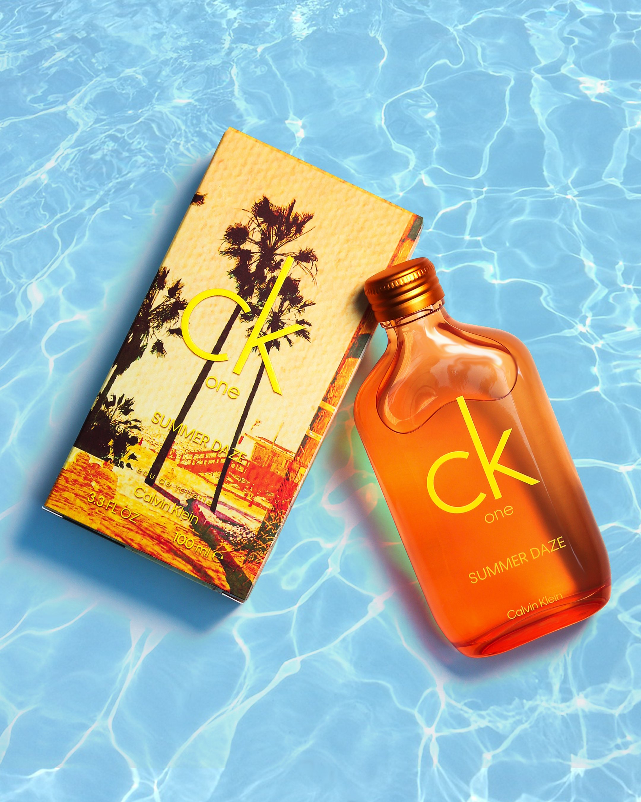 A Calvin Klein CK One Summer Daze perfume bottle and box placed in a swimming pool with light blue water.