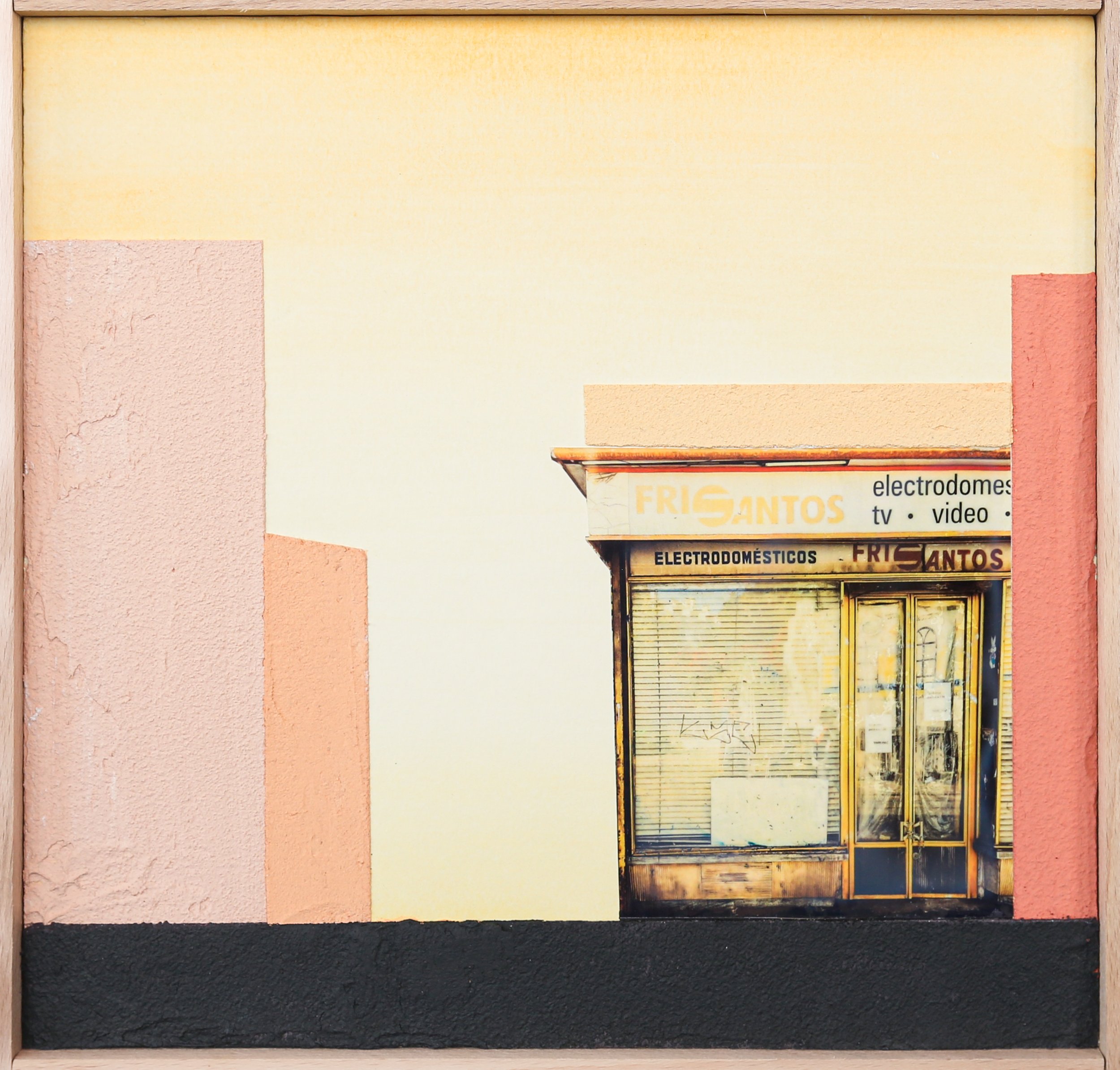 An old storefront with faded signage reading "FRI SANTOS" and "electrodomesticos"; the shop appears closed with metal shutters and a glass door, set against a pastel-colored wall with pink and peach hues. The image has a minimalist composition with a dark pavement in the foreground.