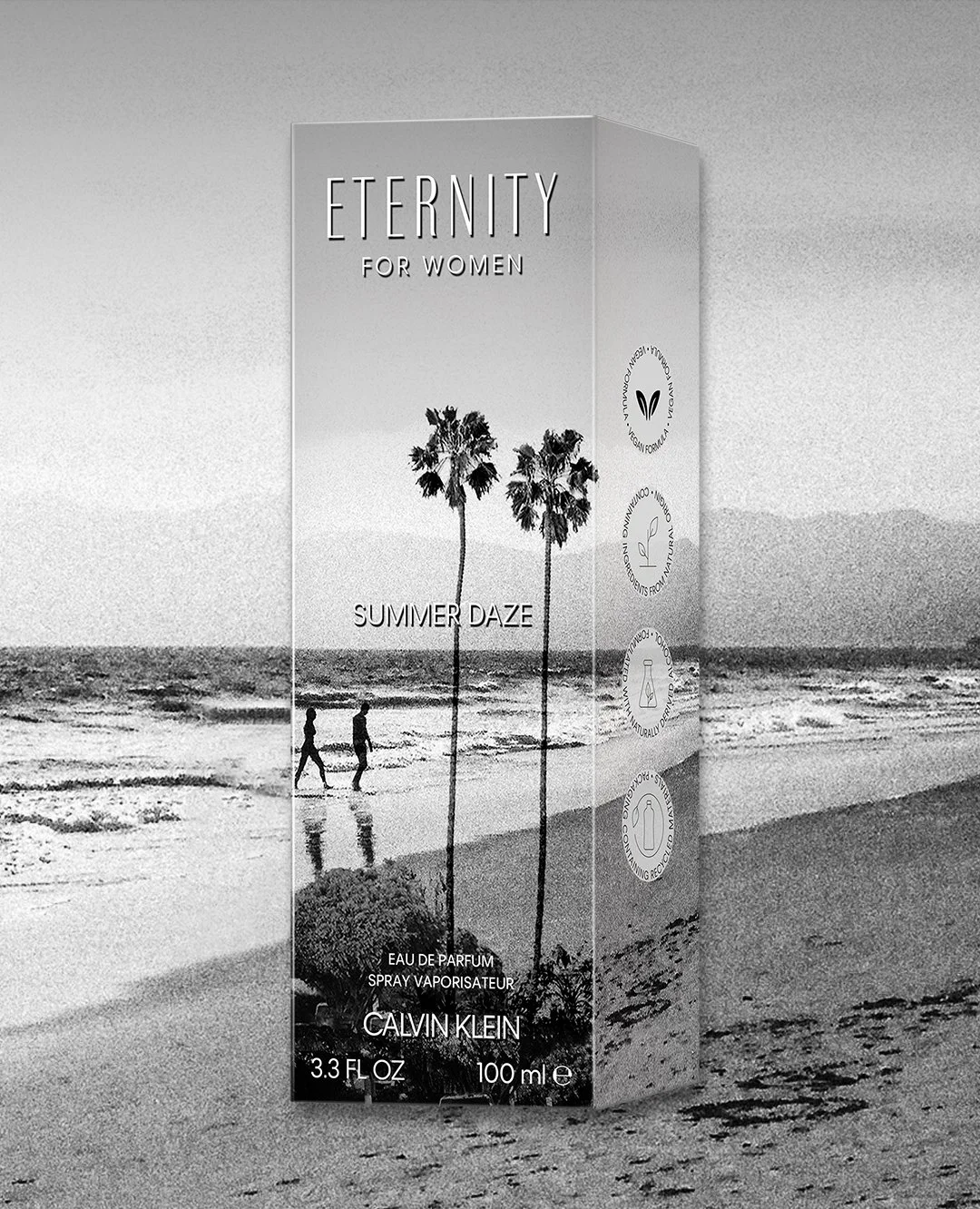 Black and white image of a perfume box labeled 'Eternity for Women' by Calvin Klein, with 'Summer Daze' scent, featuring a beach scene with two people walking and palm trees.