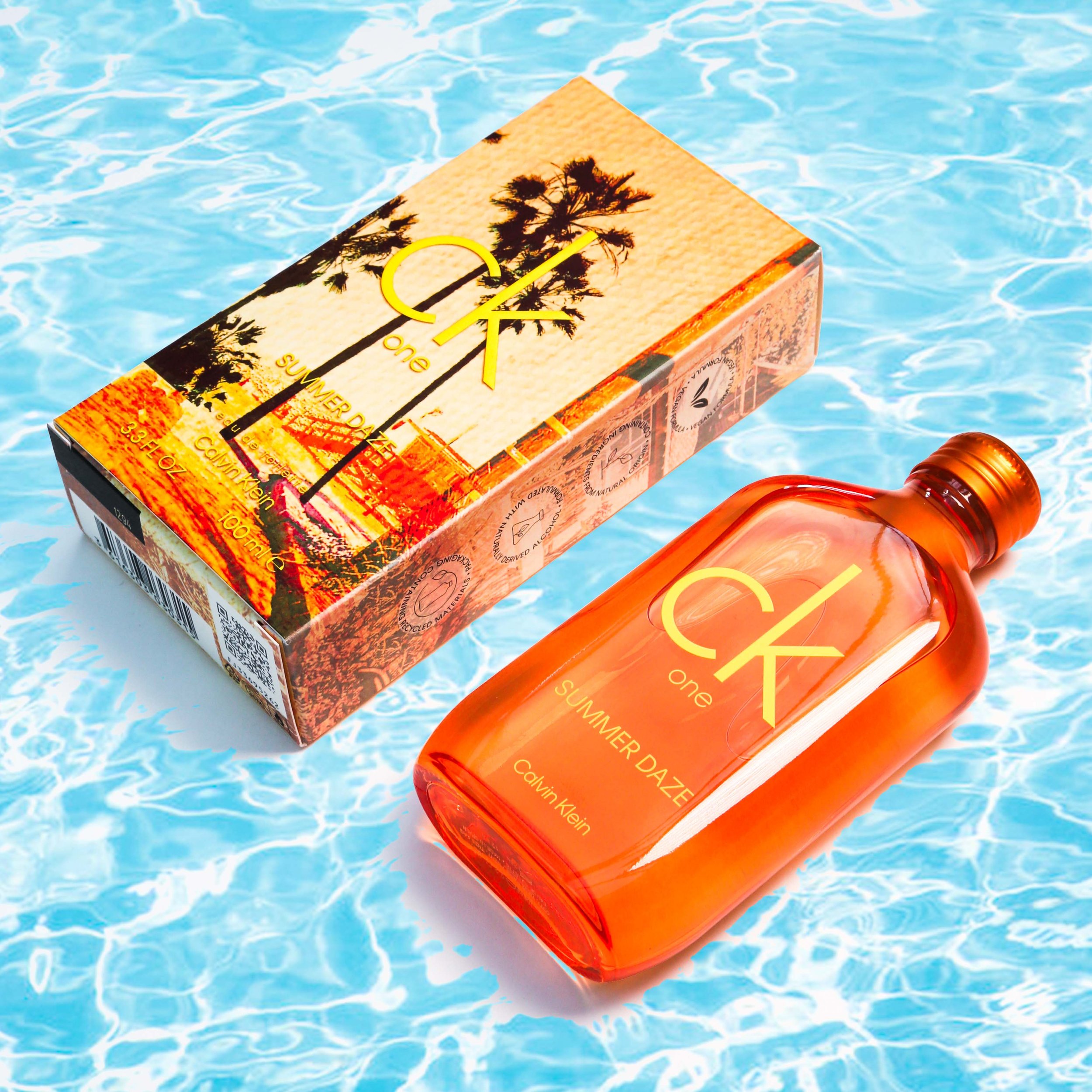 A bottle of Calvin Klein CK One Summer Daze fragrance and its packaging, placed on a blue swimming pool surface with water ripples.