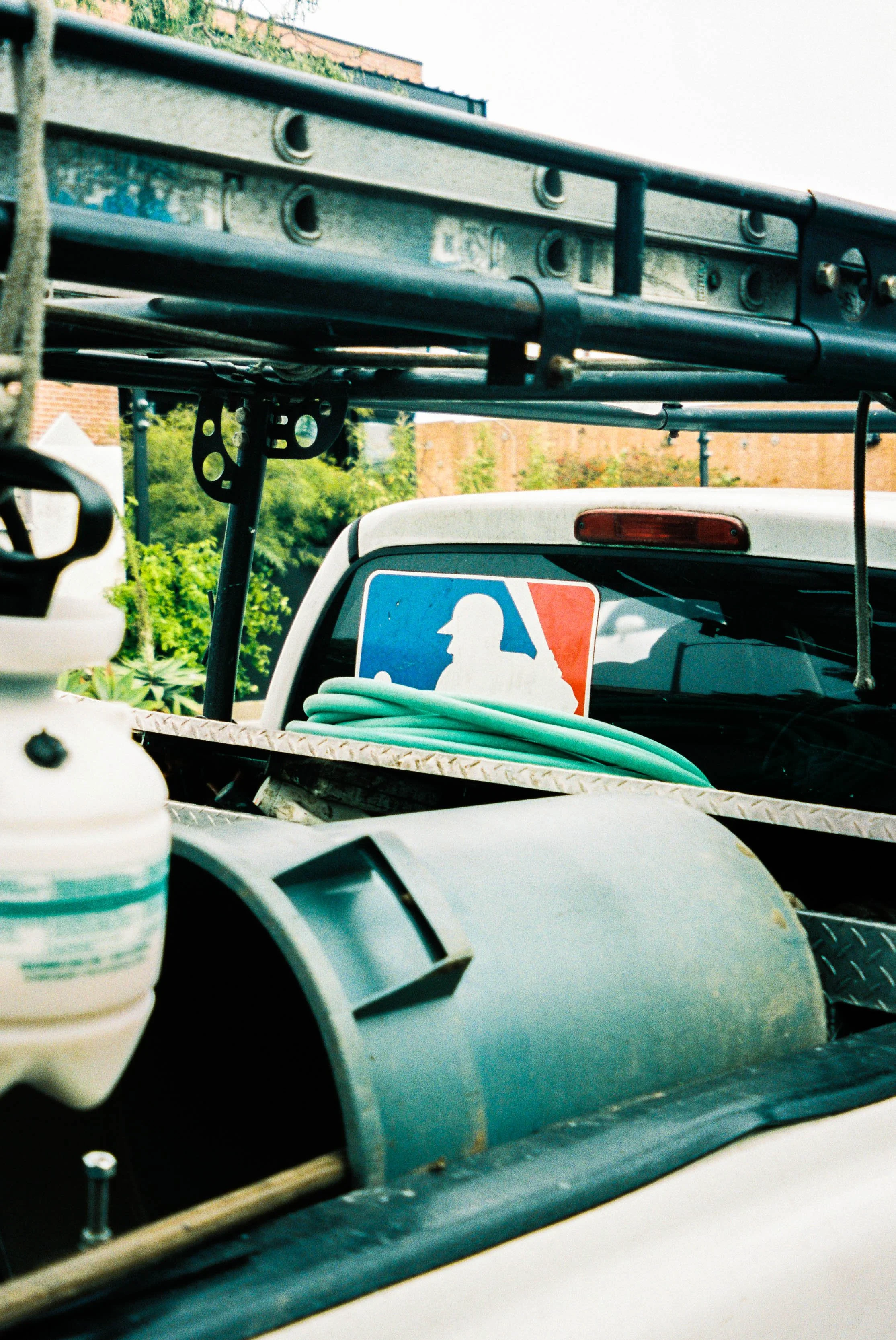 A pickup truck with a Major League Baseball logo in the back window and a coiled garden hose on the metal rack.
