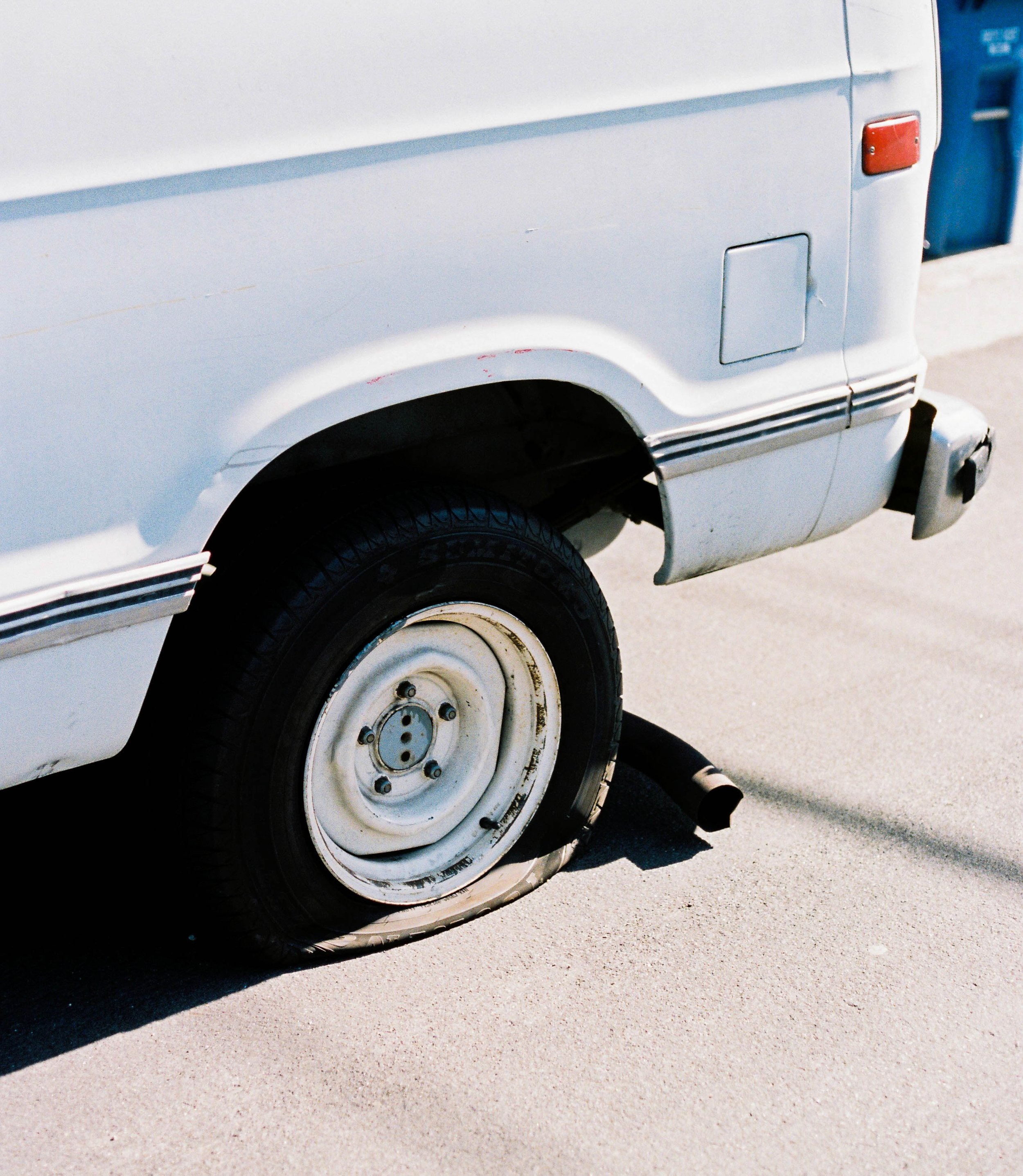 Close-up of a white van's rear wheel with a flat tire on a paved surface.