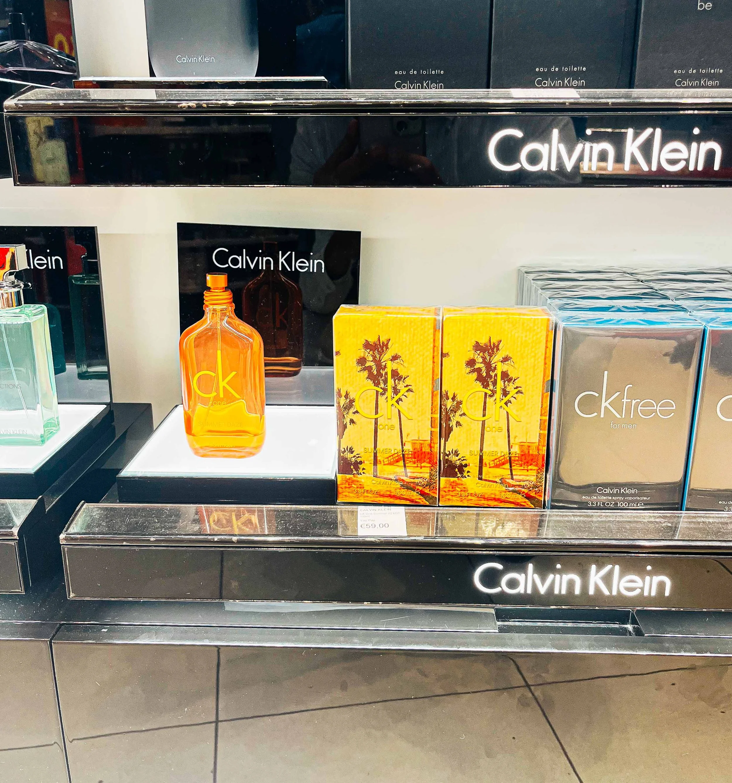 Display shelf with Calvin Klein perfume bottles and boxes, featuring orange, yellow, and gray packaging designs.